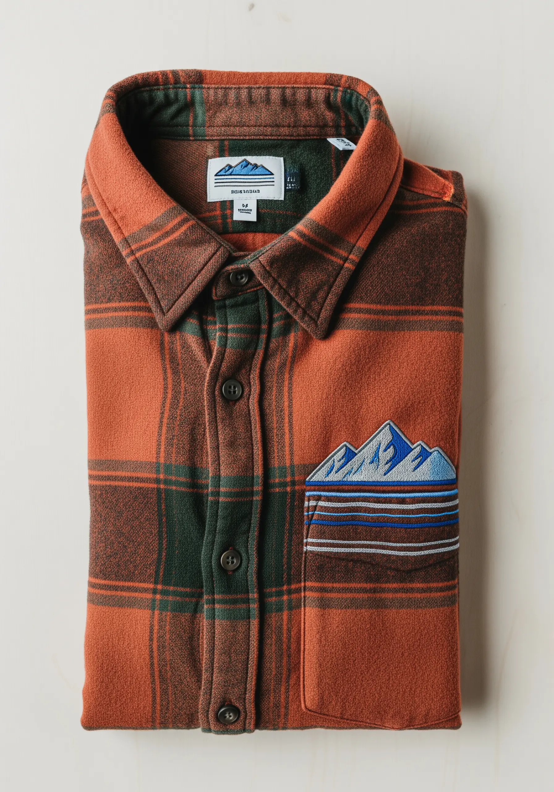 An embroidered mountain range landscape covering the pocket of an orange flannel shirt.