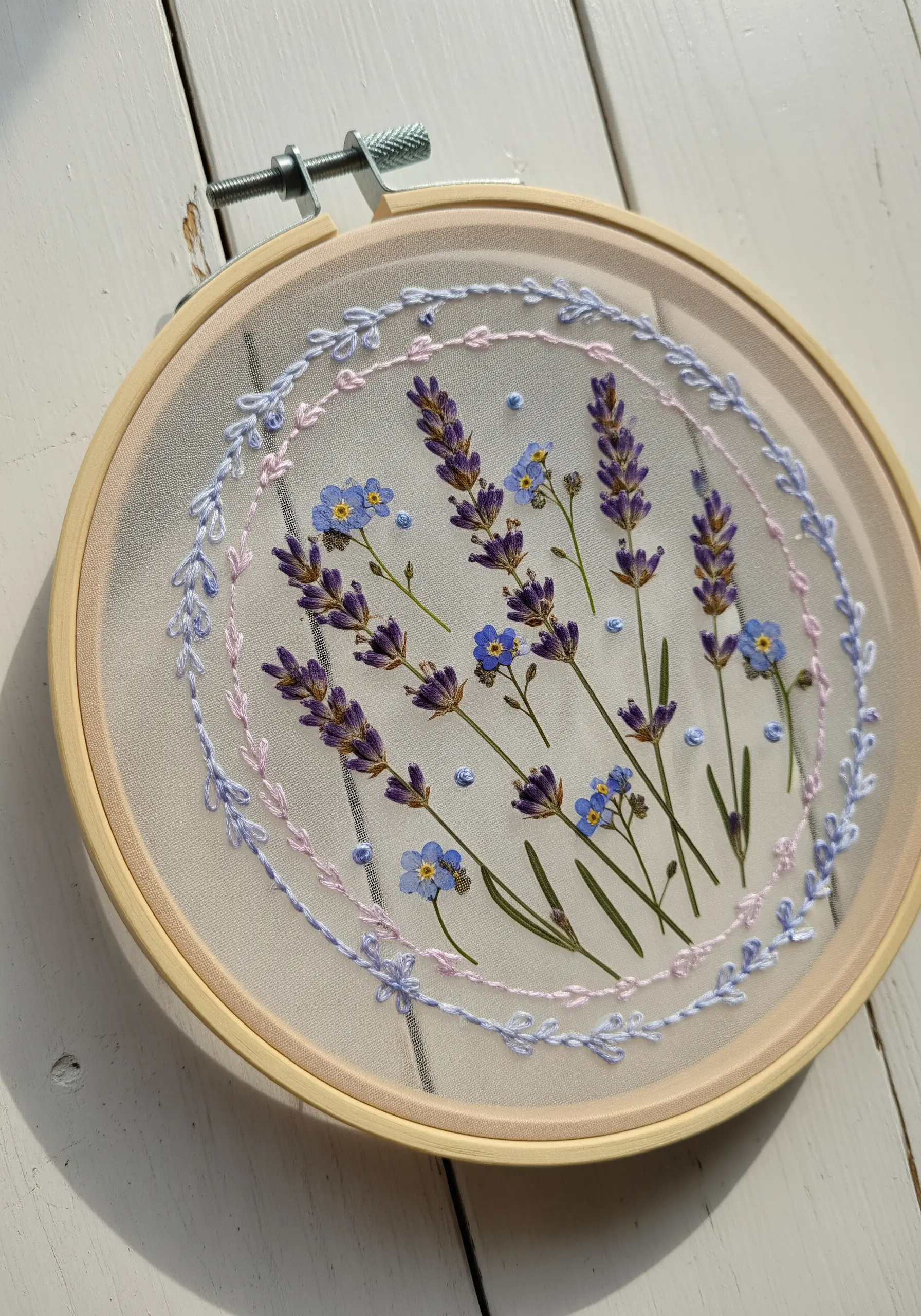 Pressed lavender and forget-me-nots with a pastel stitched border on sheer fabric.