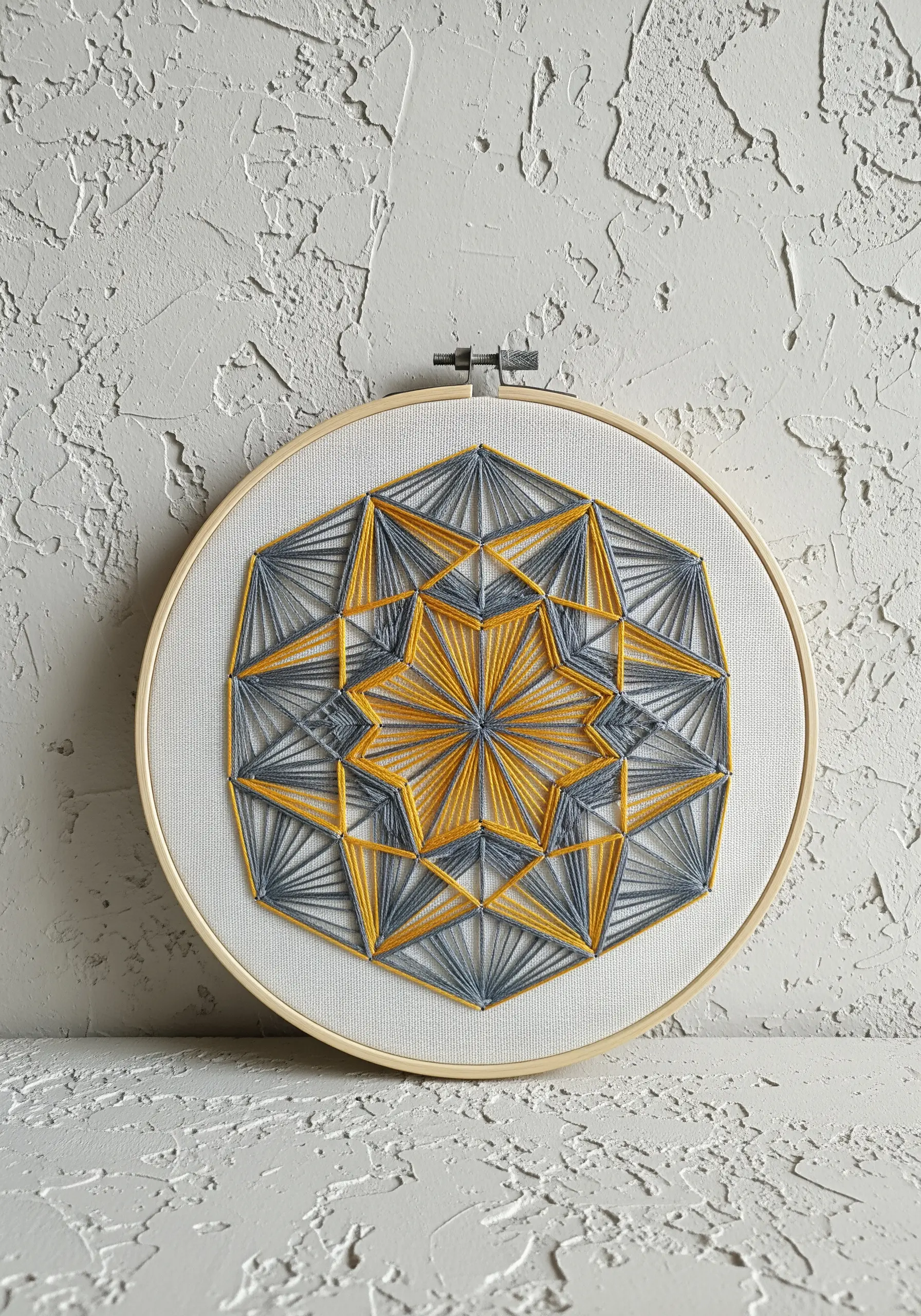 A geometric string-art style mandala in grey and yellow on white fabric.