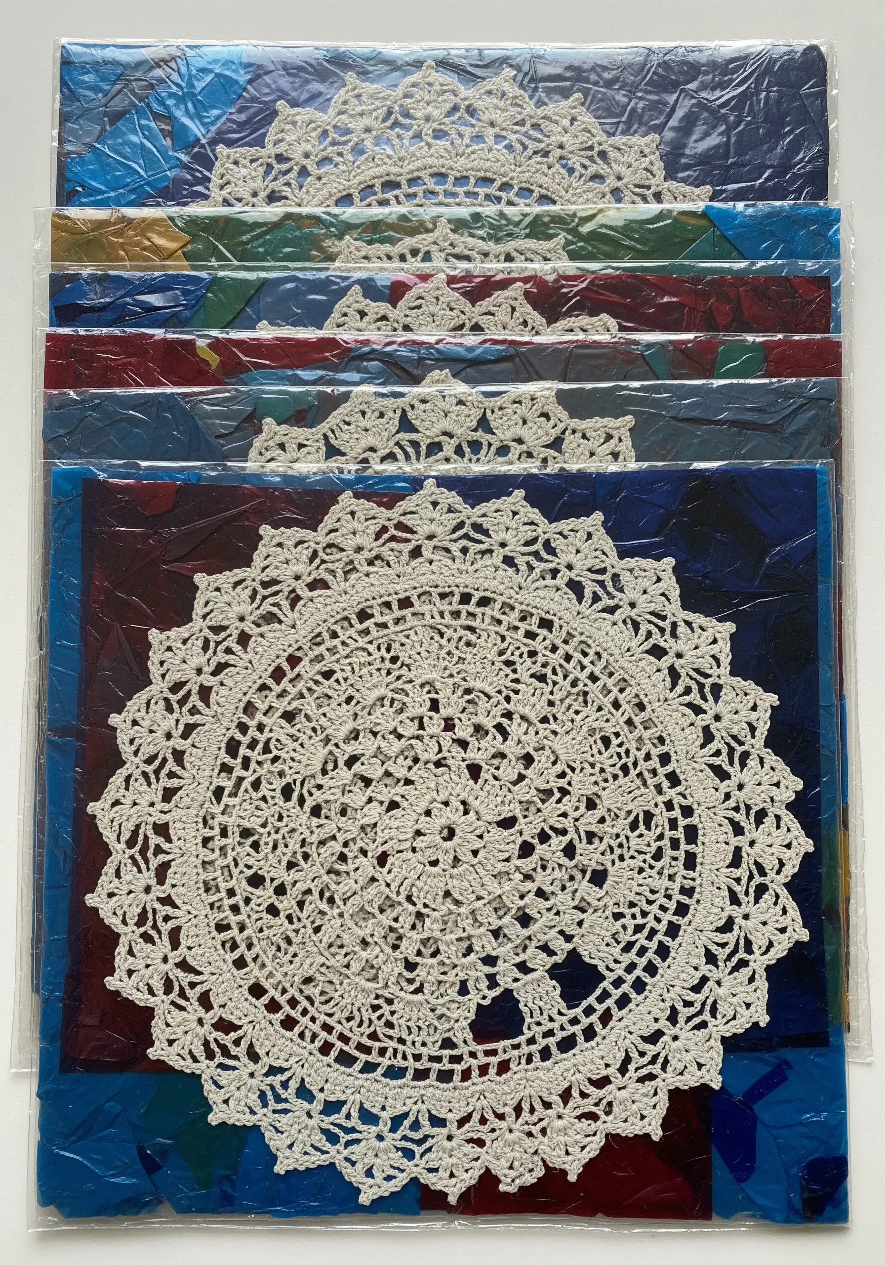 White crochet doilies of various sizes layered over vibrant, abstract painted backgrounds in clear sleeves.