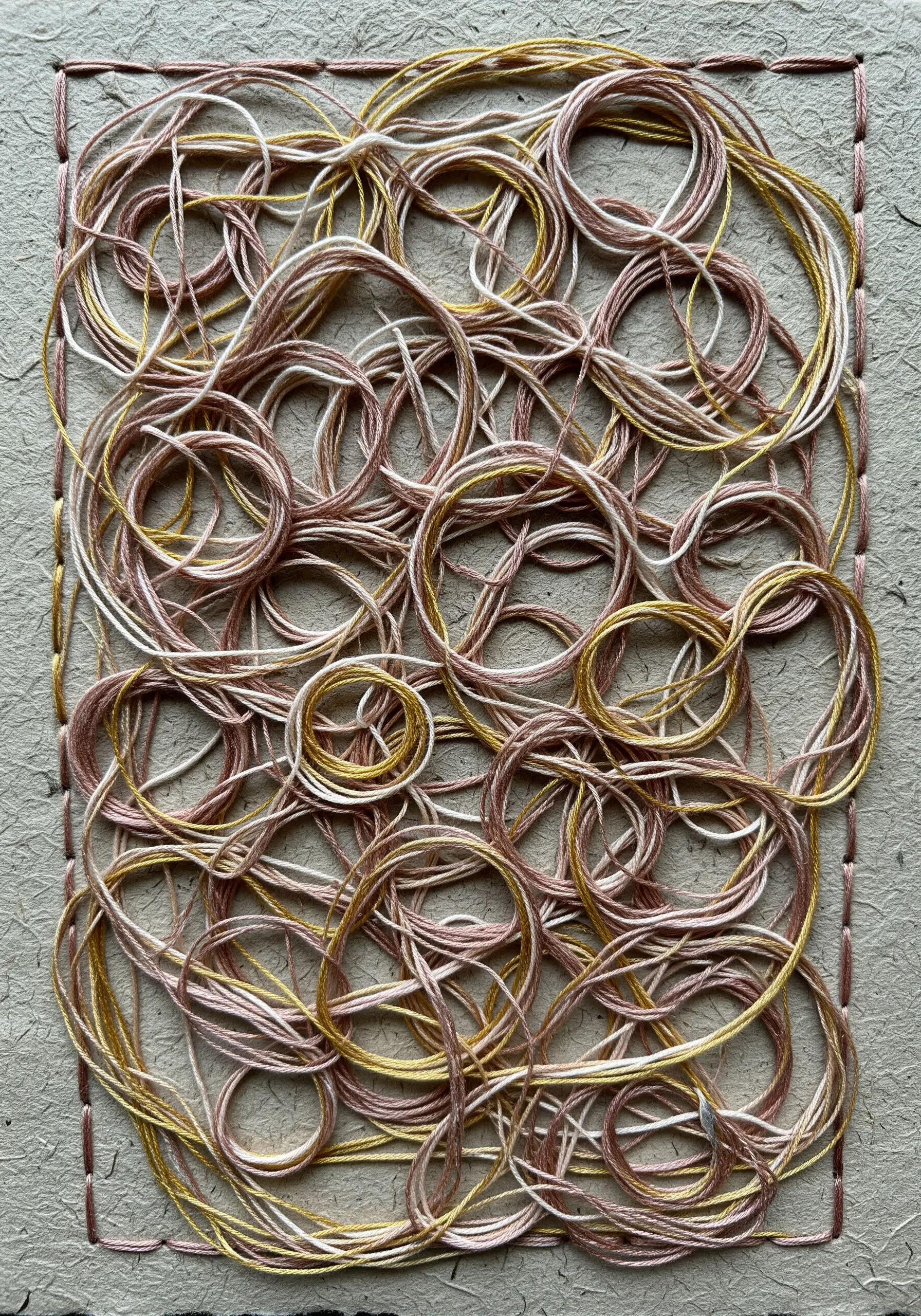 Overlapping circles of pink, white, and gold thread stitched onto a piece of kraft paper