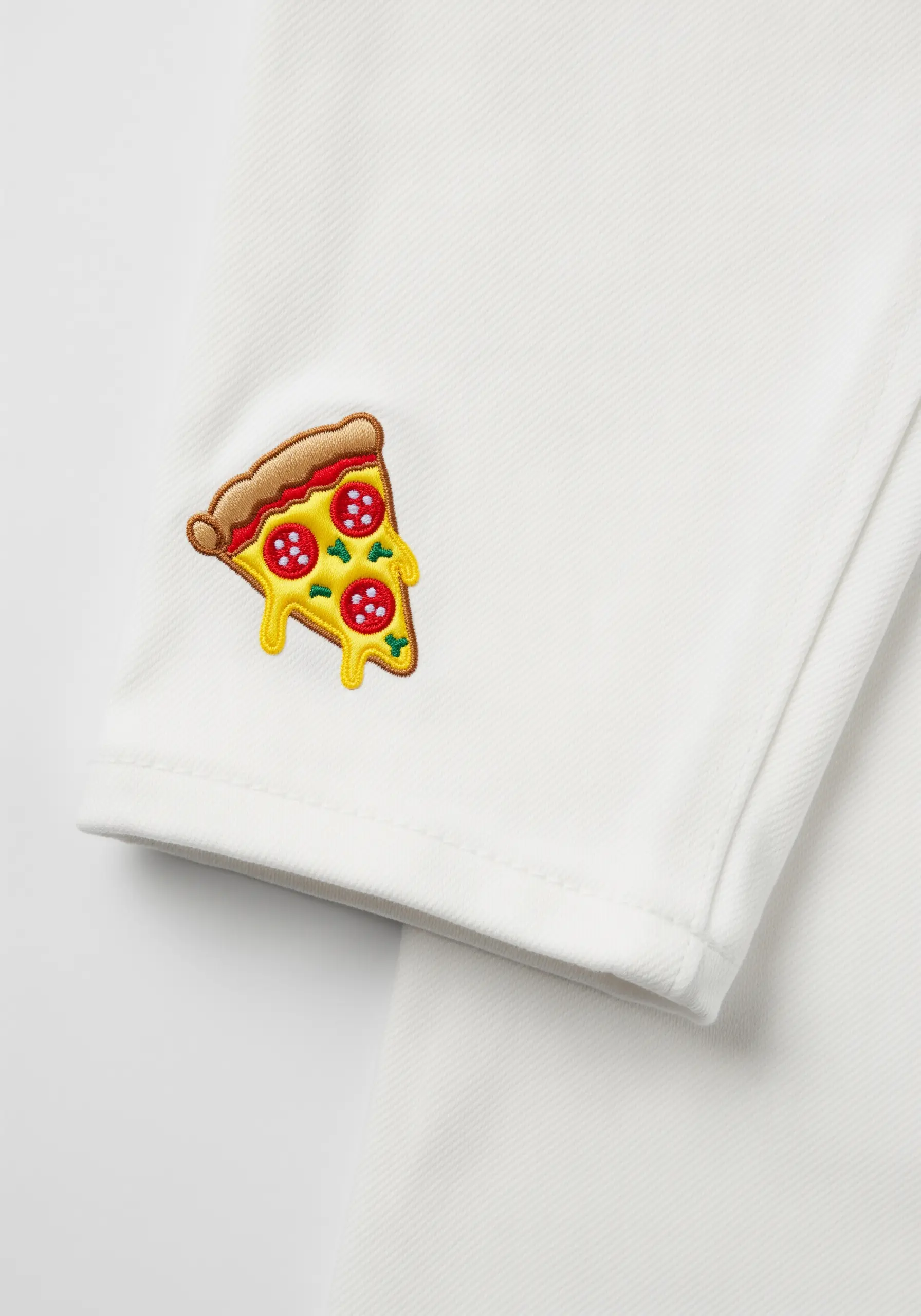 A whimsical embroidered slice of pizza with layered toppings on the cuff of white jeans.
