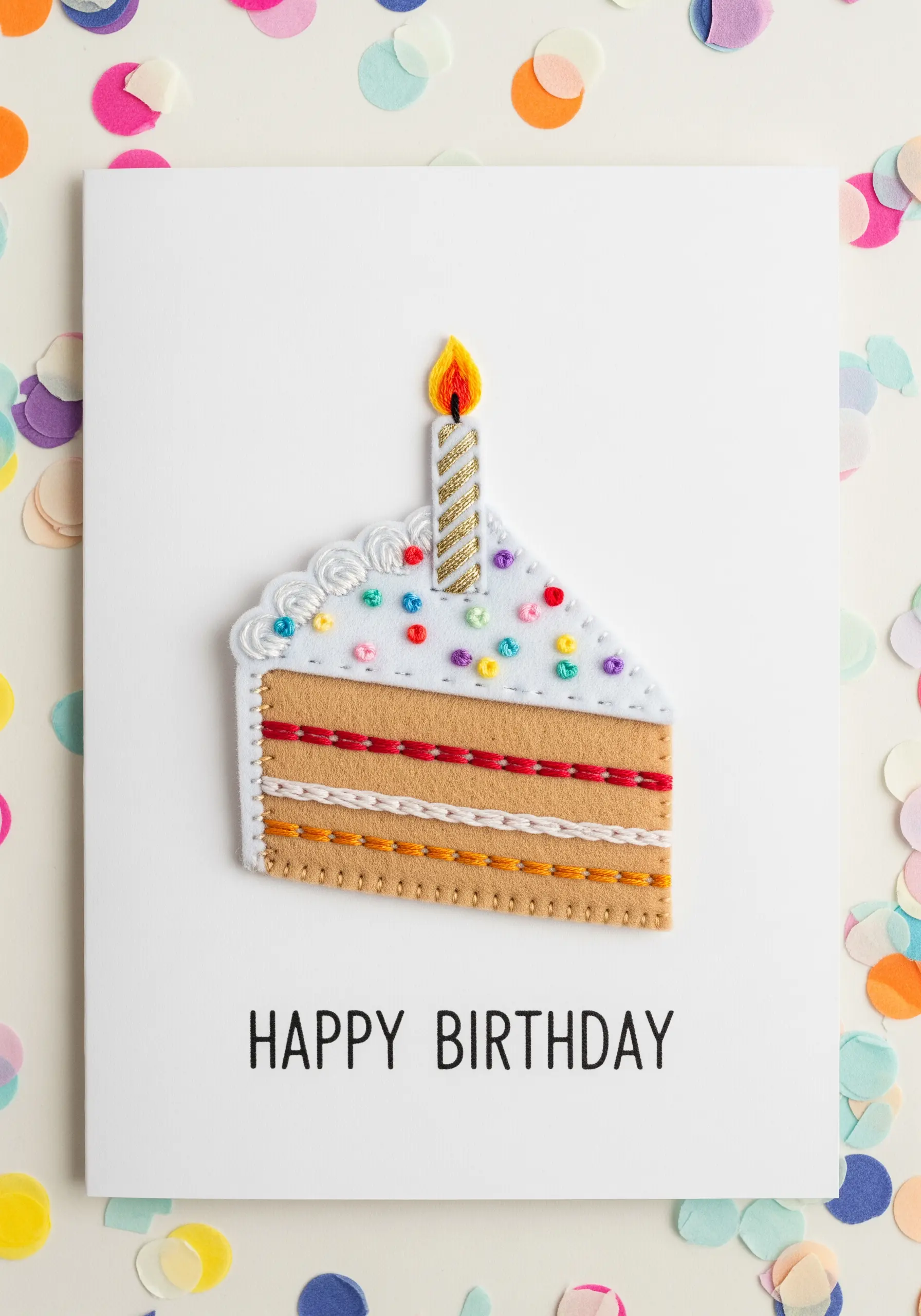 A birthday card featuring a cake slice made from layered felt and decorative embroidery stitches.