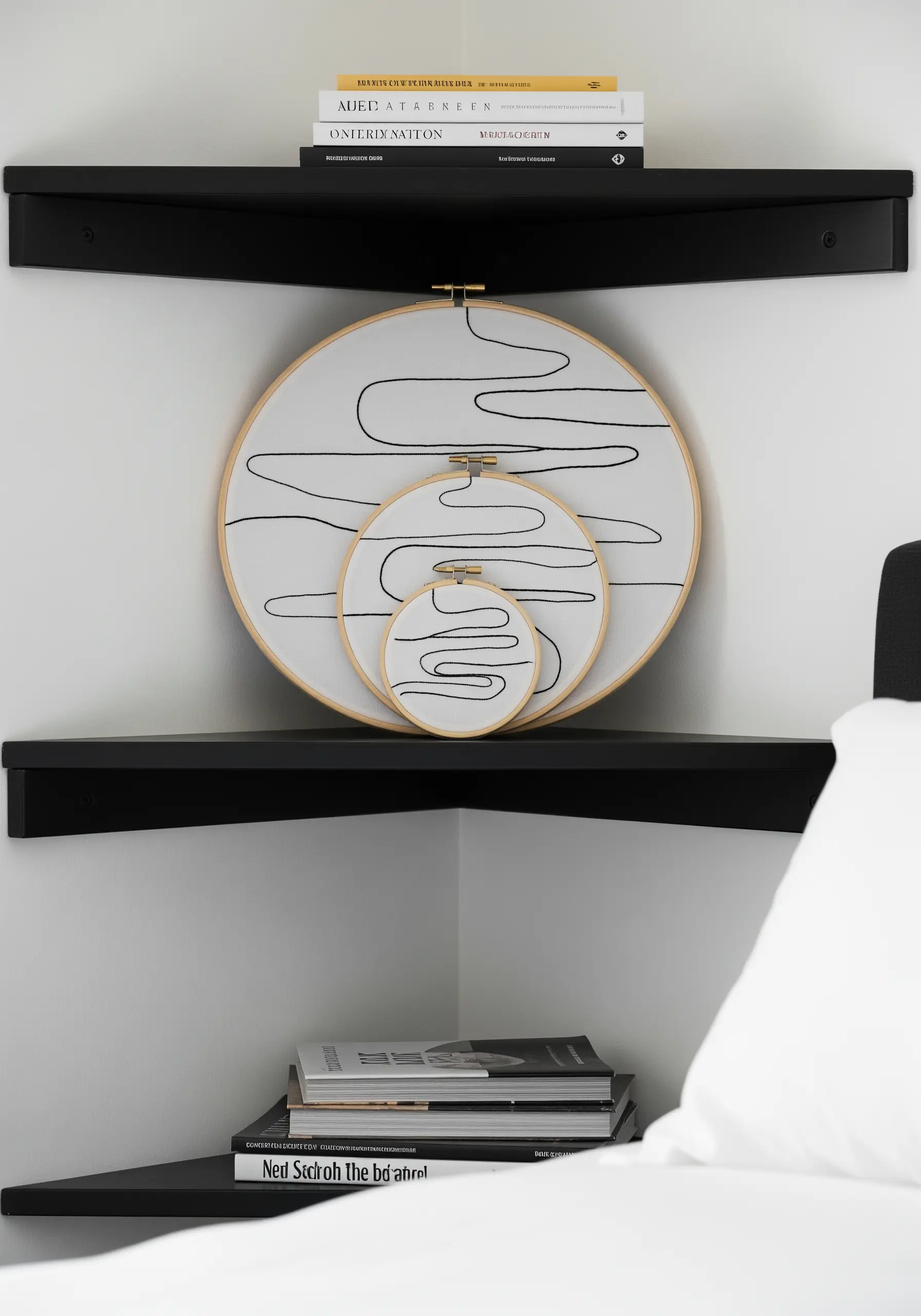 Three nested embroidery hoops with a continuous abstract black line, displayed on a corner shelf.