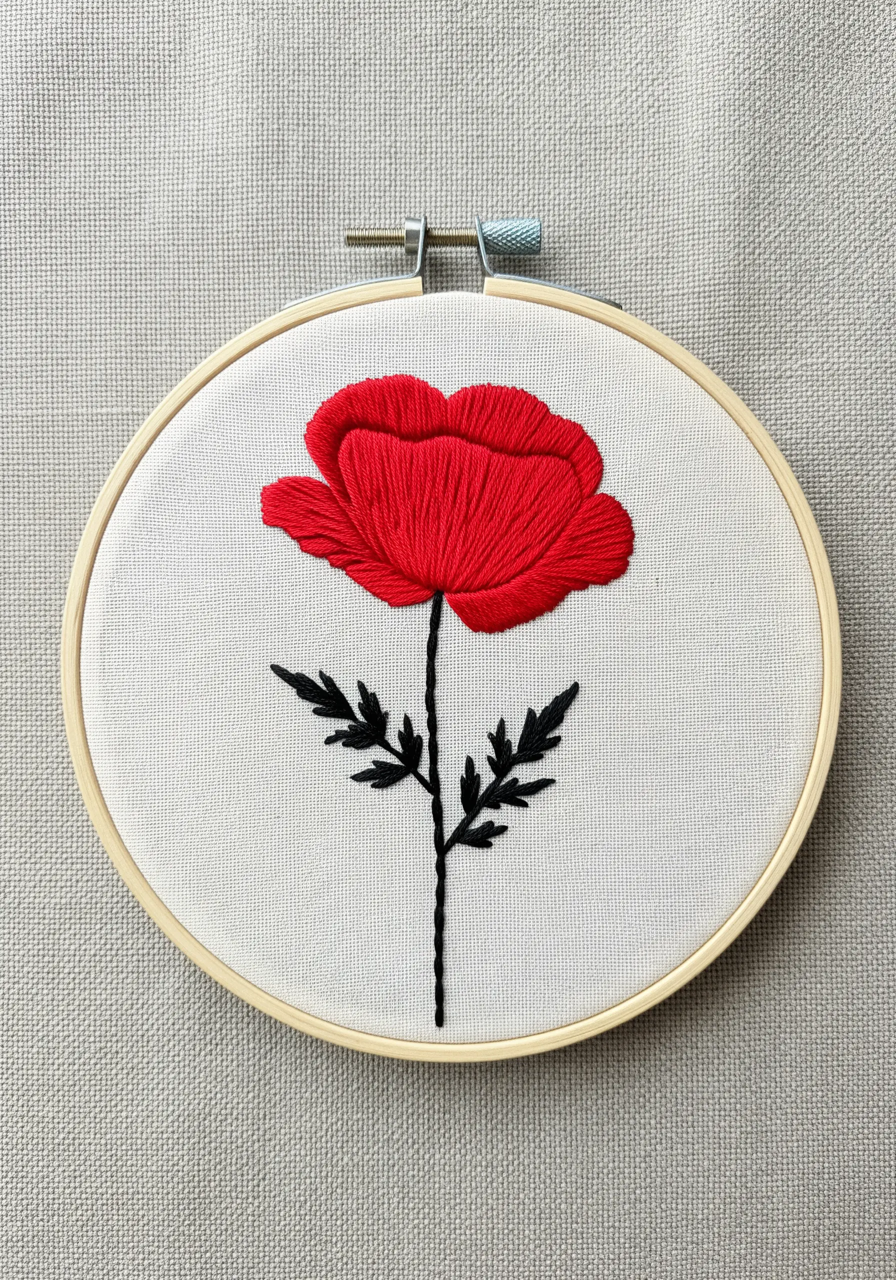 A vibrant red poppy with layered petals embroidered against a white background.