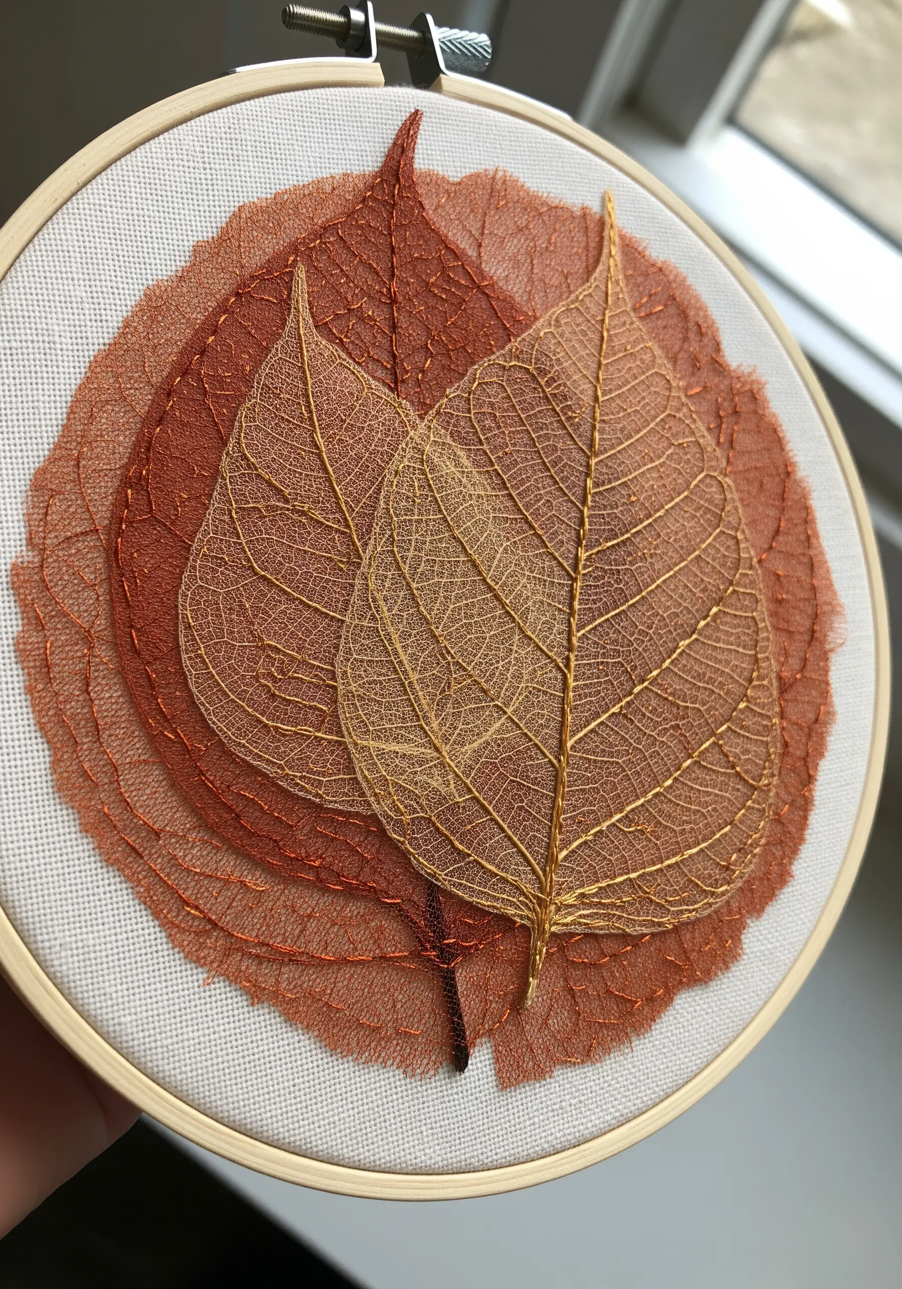A collage of delicate, transparent skeleton leaves stitched onto fabric in warm tones.