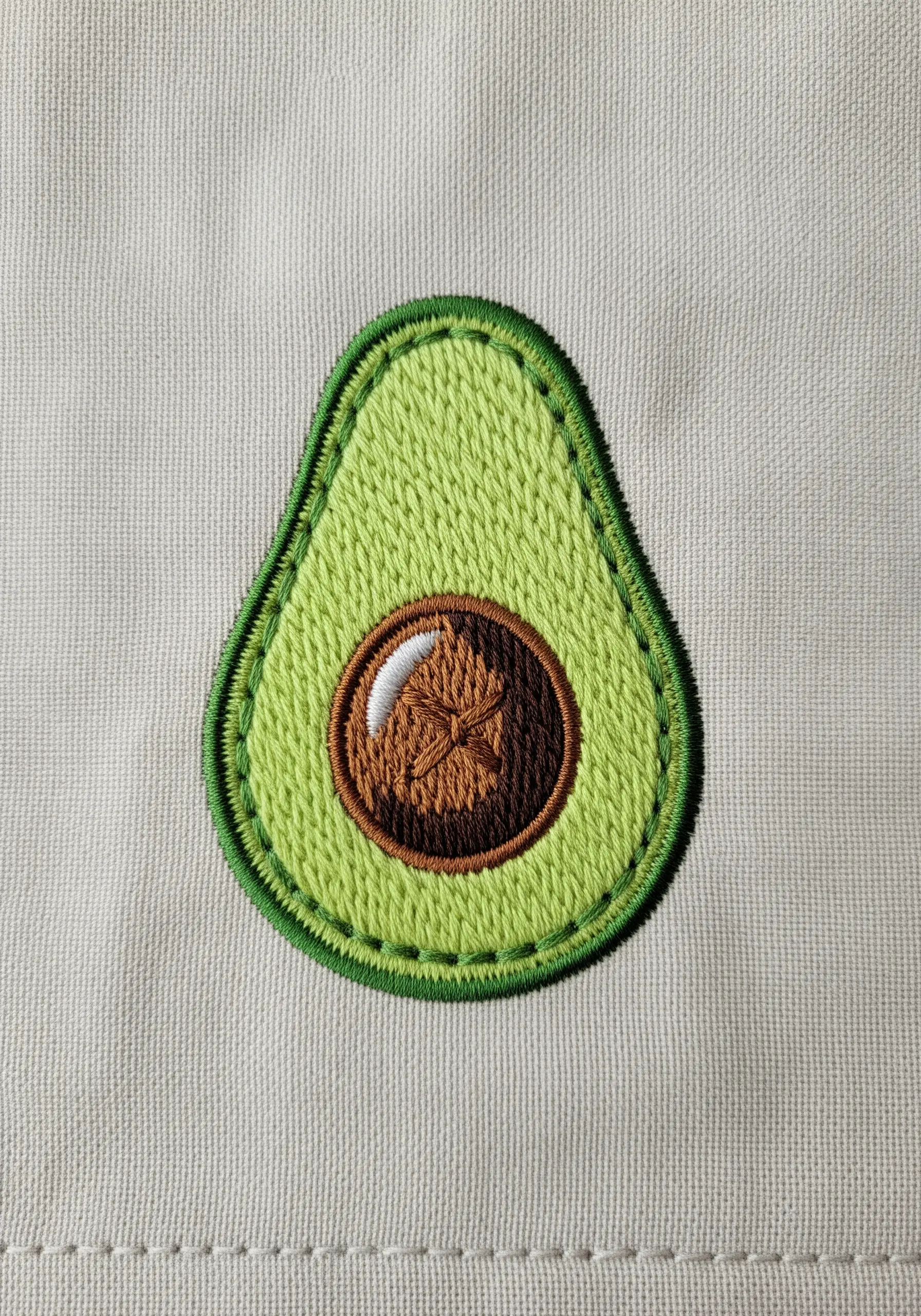 A detailed embroidery of an avocado half with a textured pit and a layered outline.