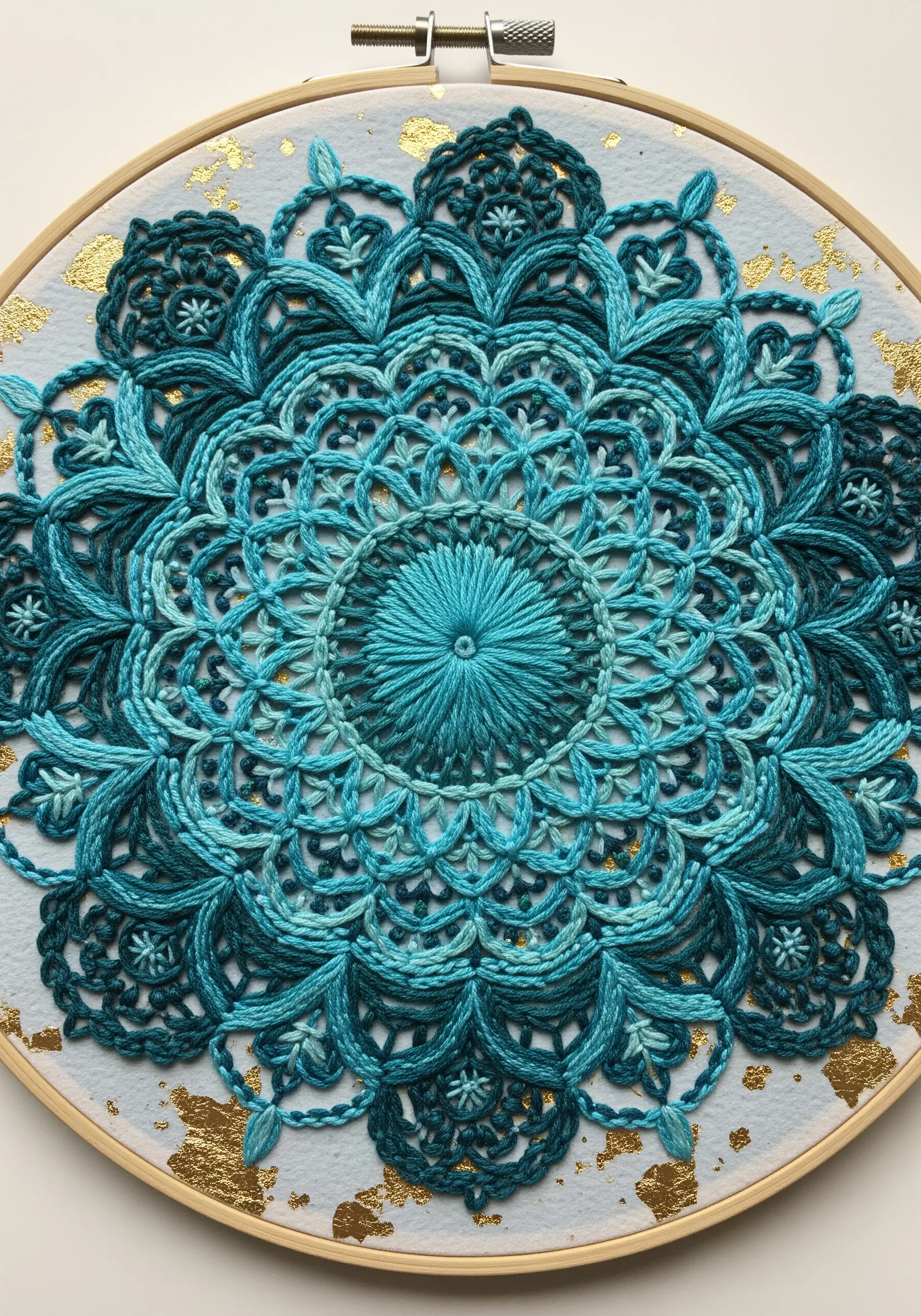 Intricate blue embroidered mandala on paper with gold leaf accents.
