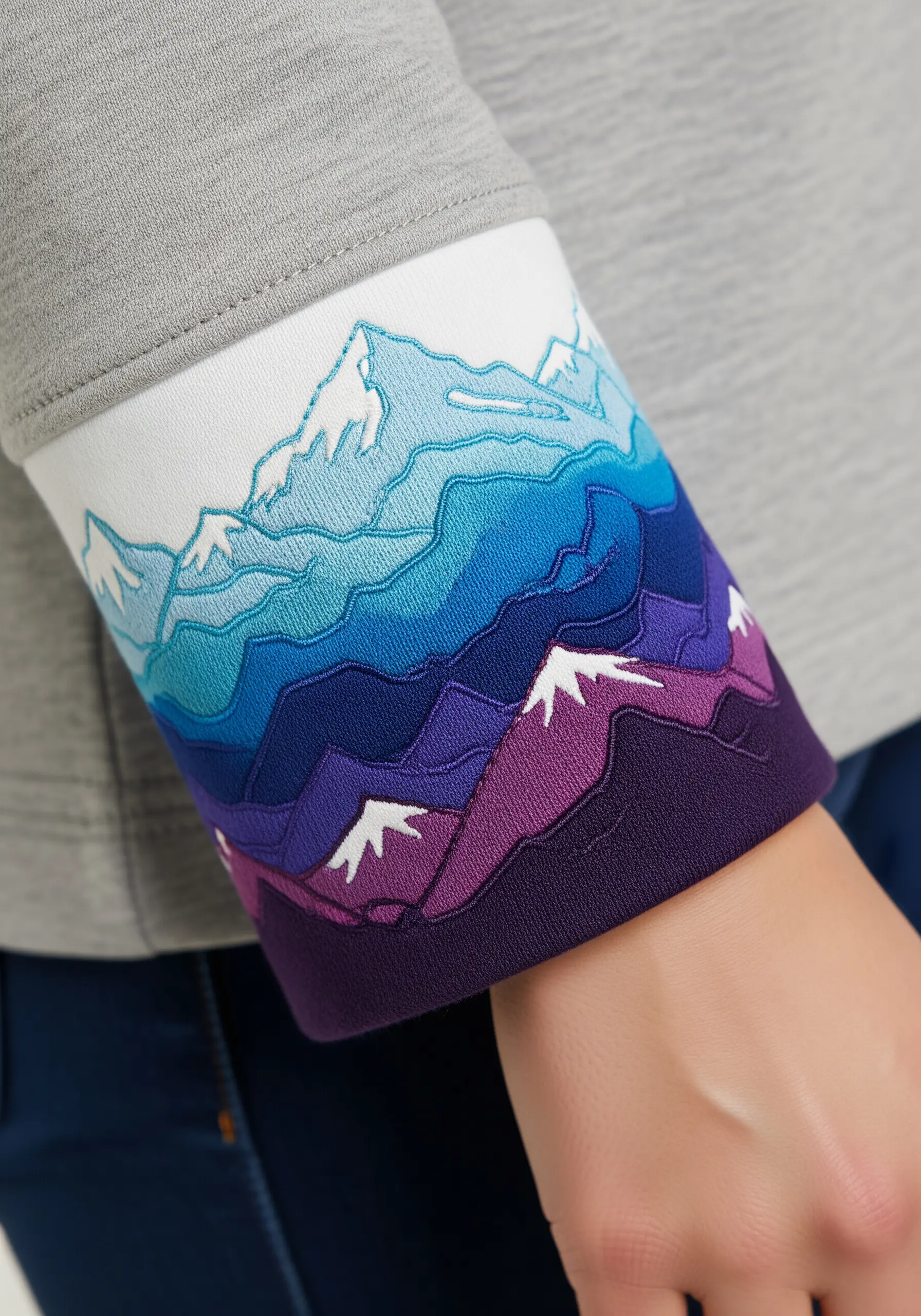 A layered fabric appliqué of a mountain range in shades of purple and blue on a sweatshirt cuff.