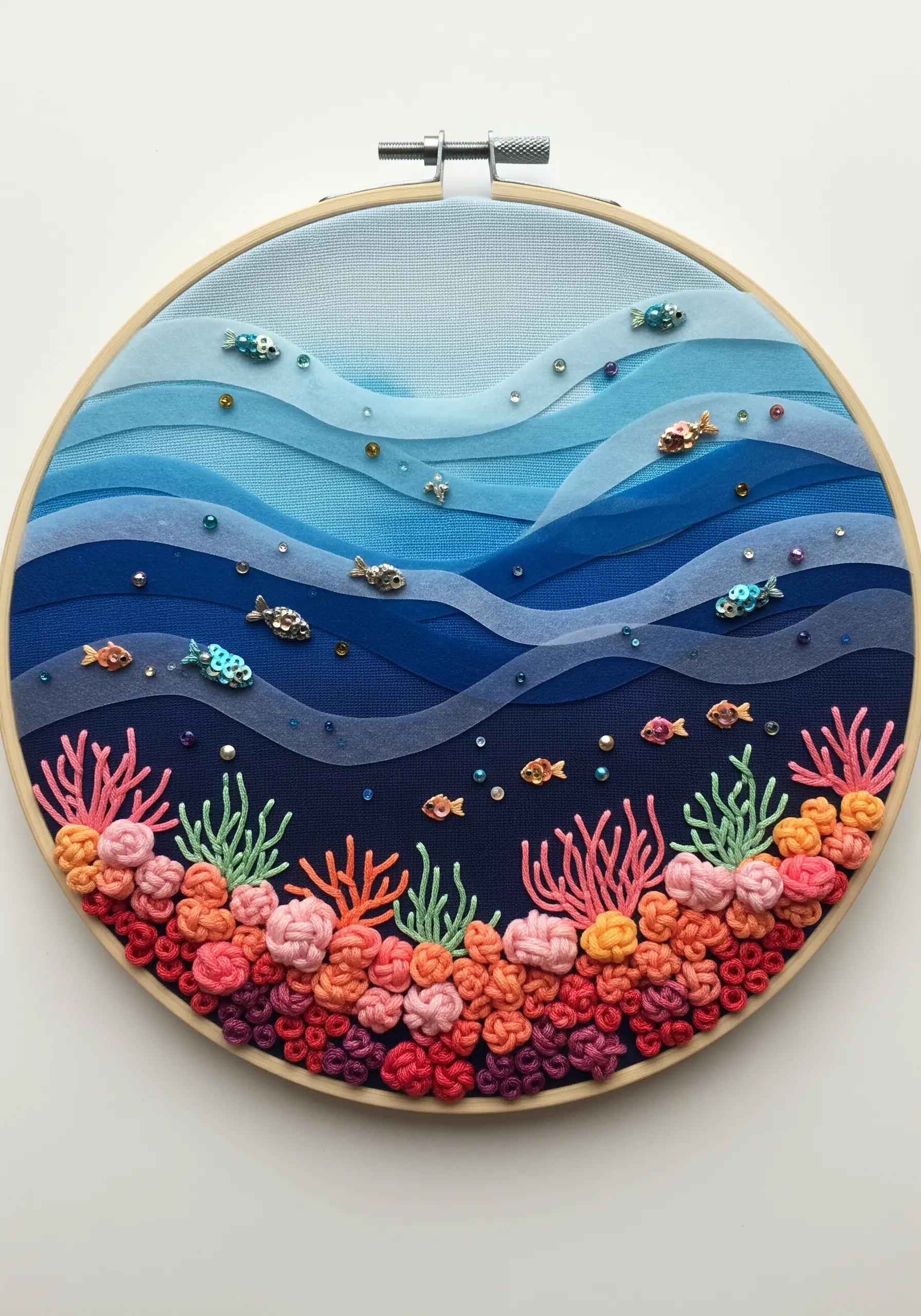 Embroidery hoop with layered blue organza for water and a textured coral reef of French knots.
