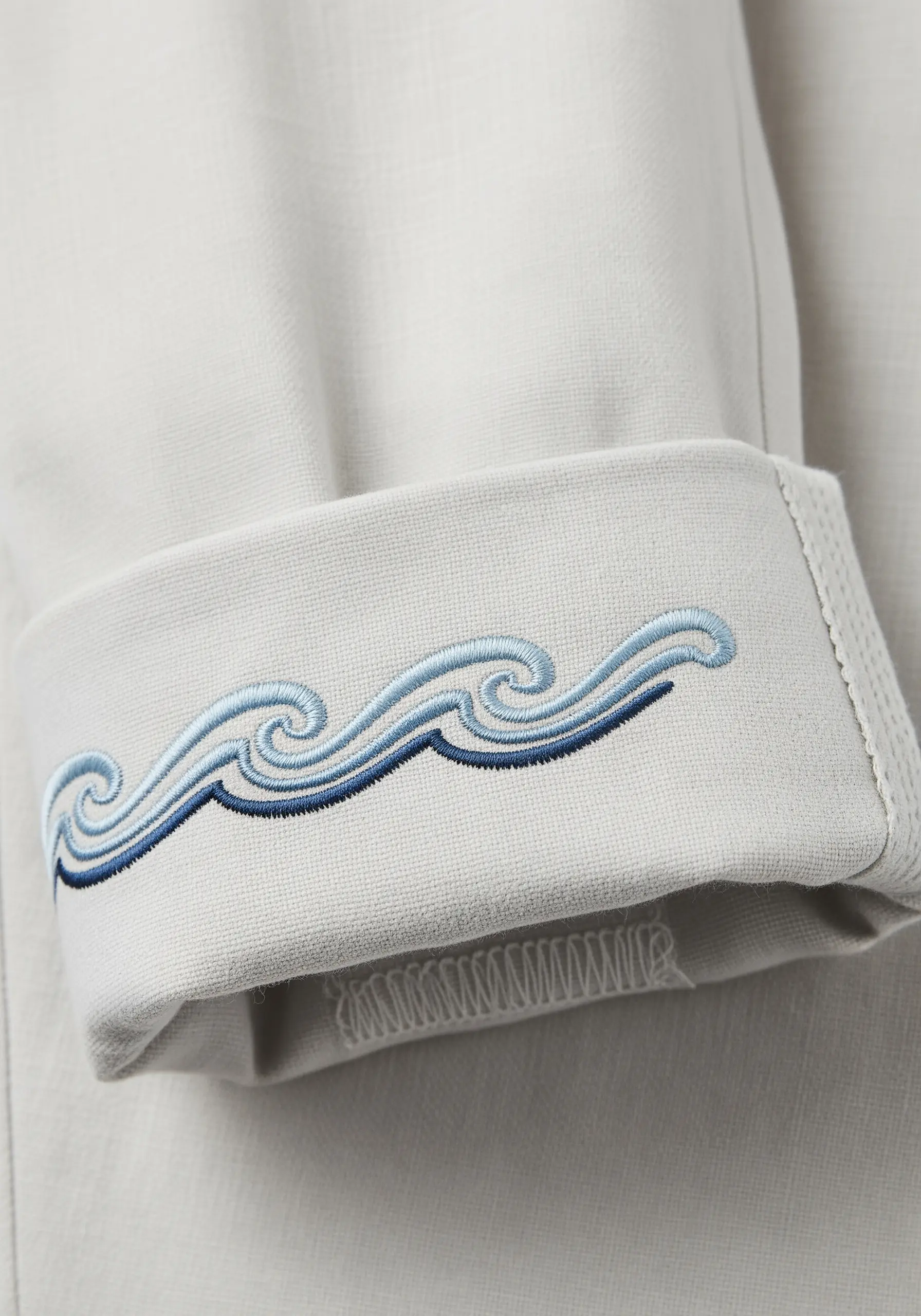 Stylized waves in shades of blue embroidered on a sleeve cuff using raised stitches.