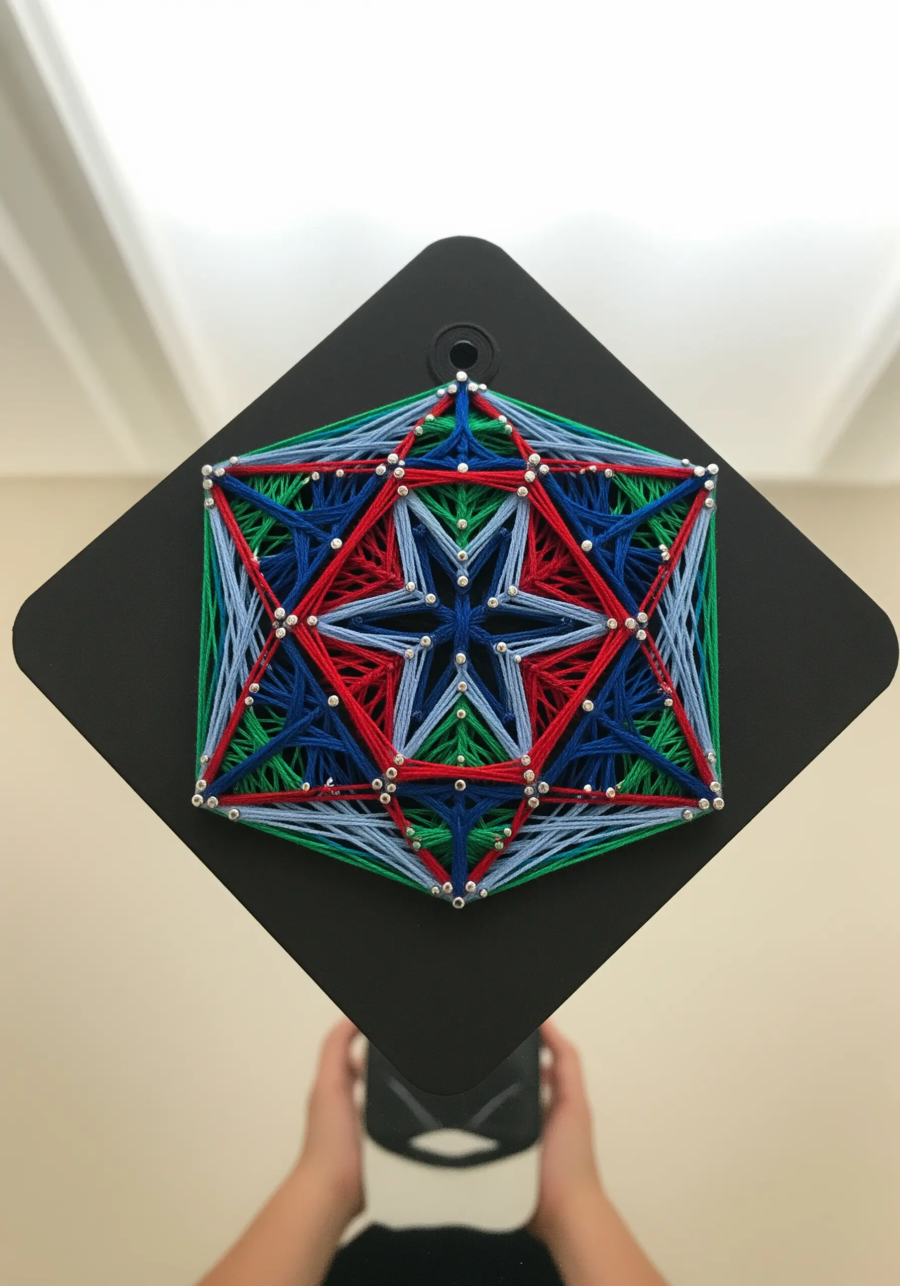 A complex geometric mandala string art in red, blue, and green.