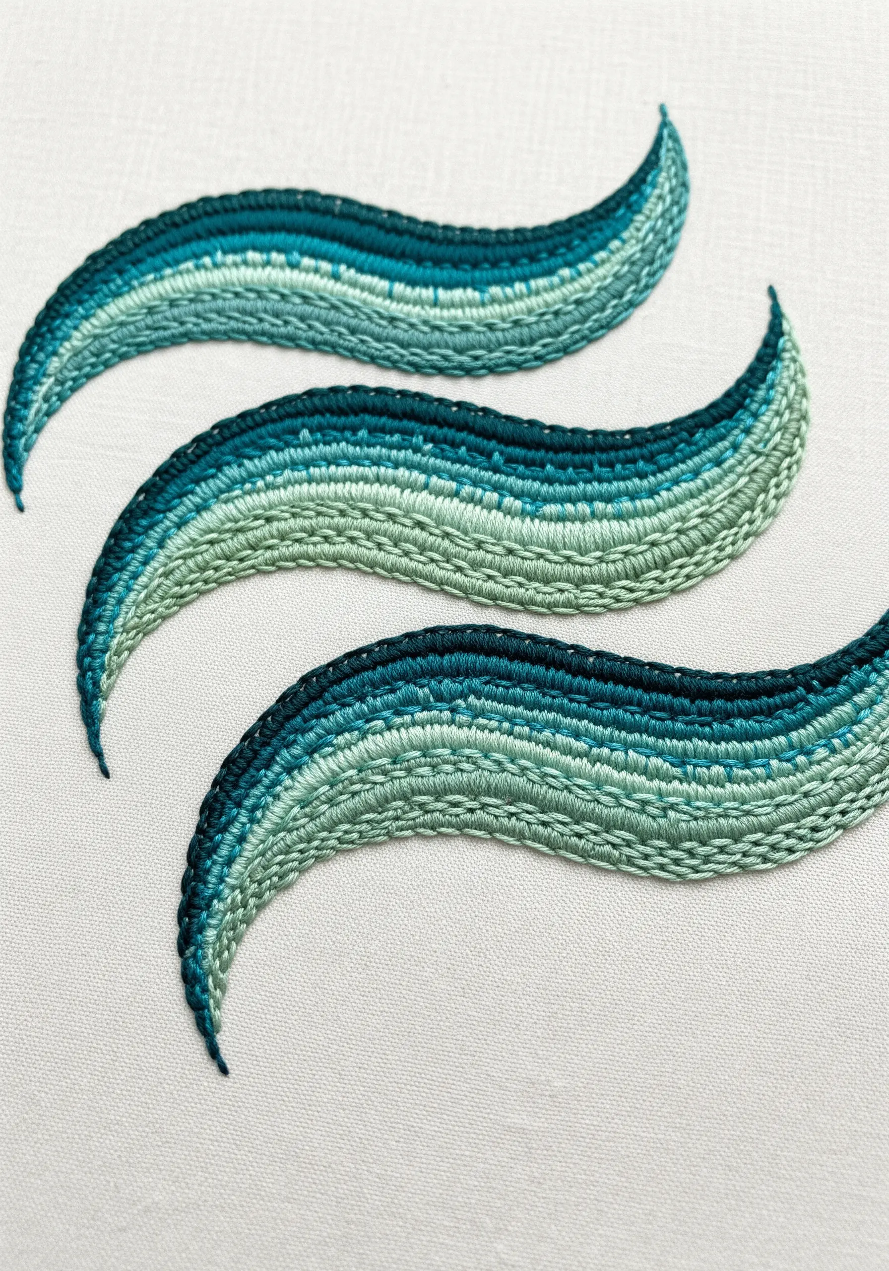 Three embroidered waves with tonal blue and green satin stitch bands.