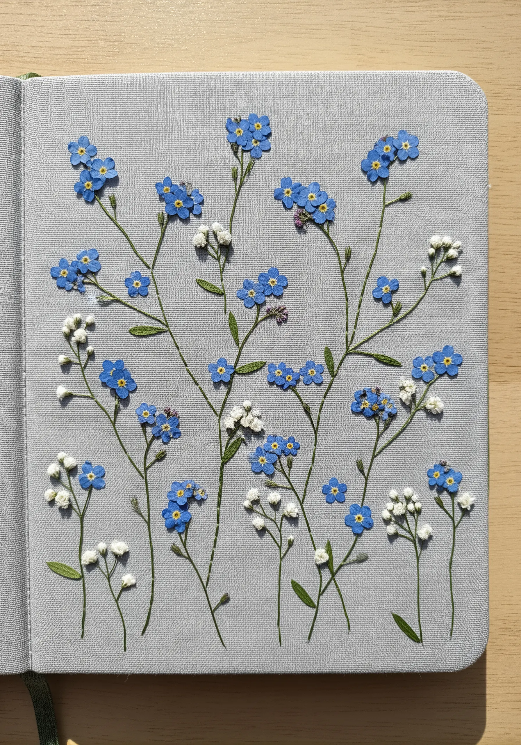 Pressed forget-me-nots and baby's breath arranged on a grey journal page.