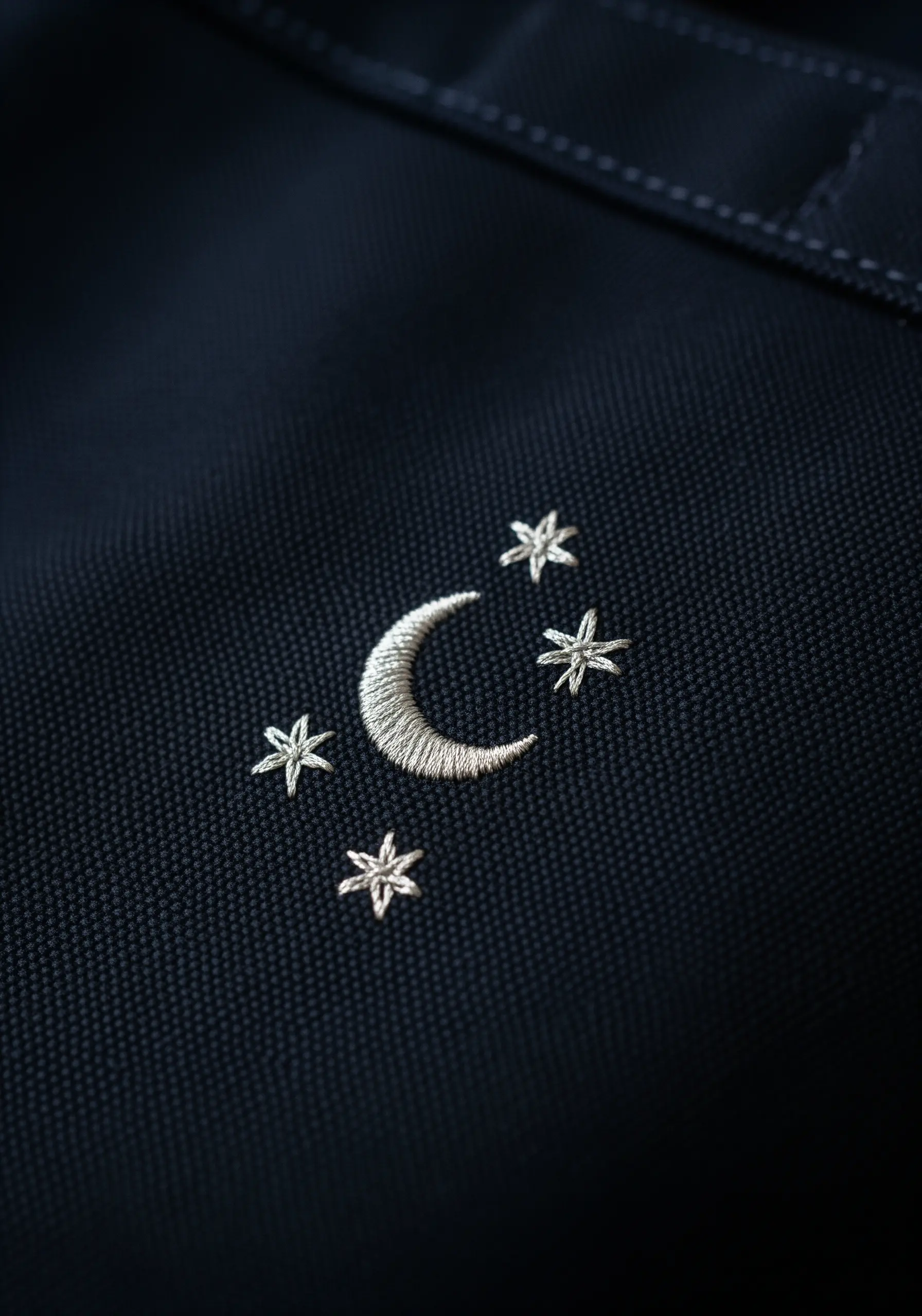 A small satin-stitched crescent moon and stars embroidered on dark navy fabric.