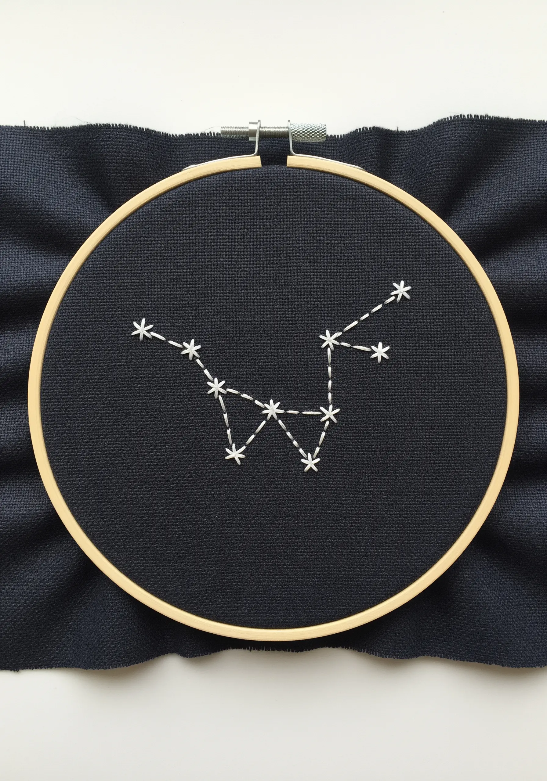 The Cassiopeia constellation stitched in white thread on a dark navy blue fabric.