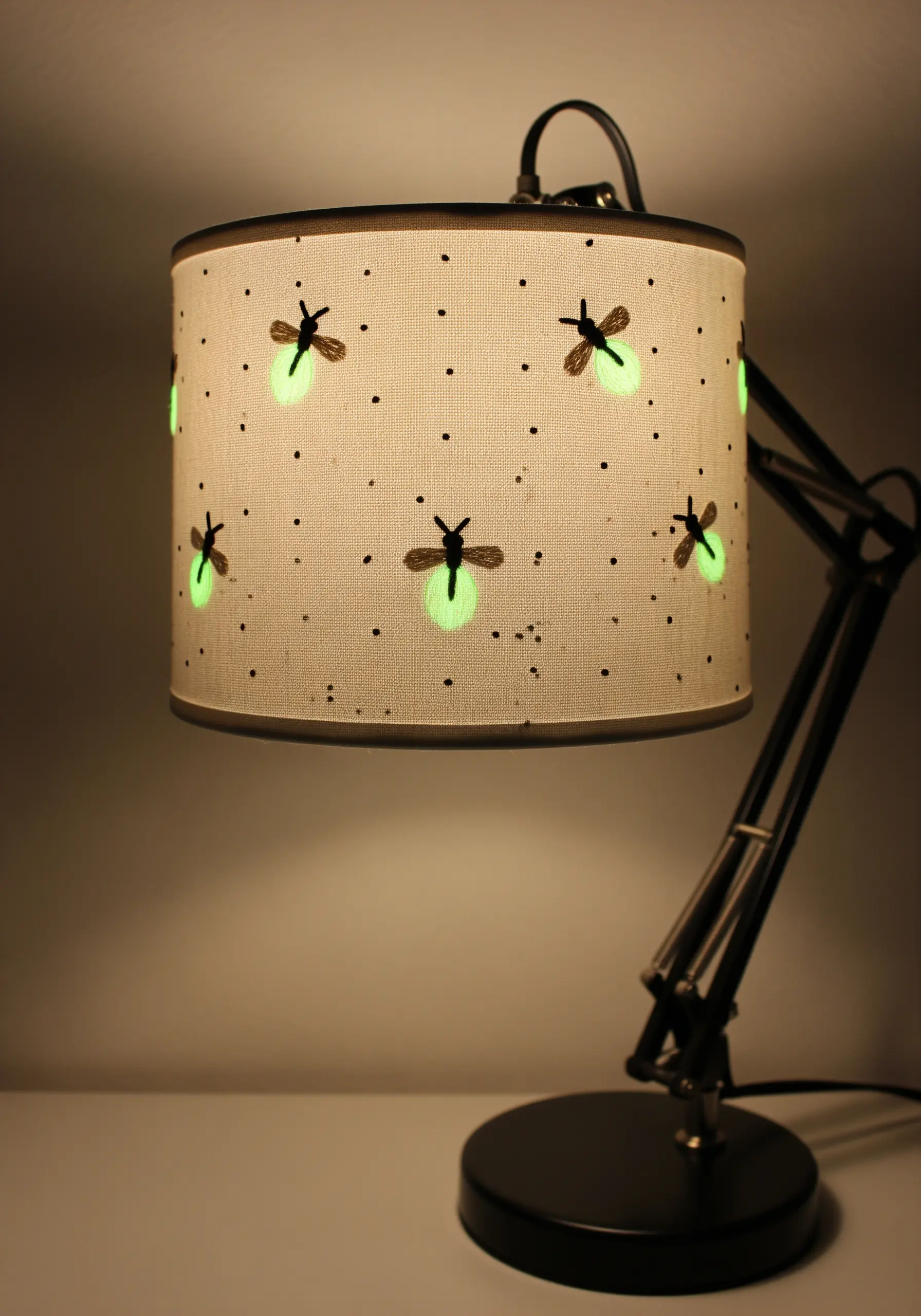A lampshade with embroidered fireflies that have glow-in-the-dark bodies.