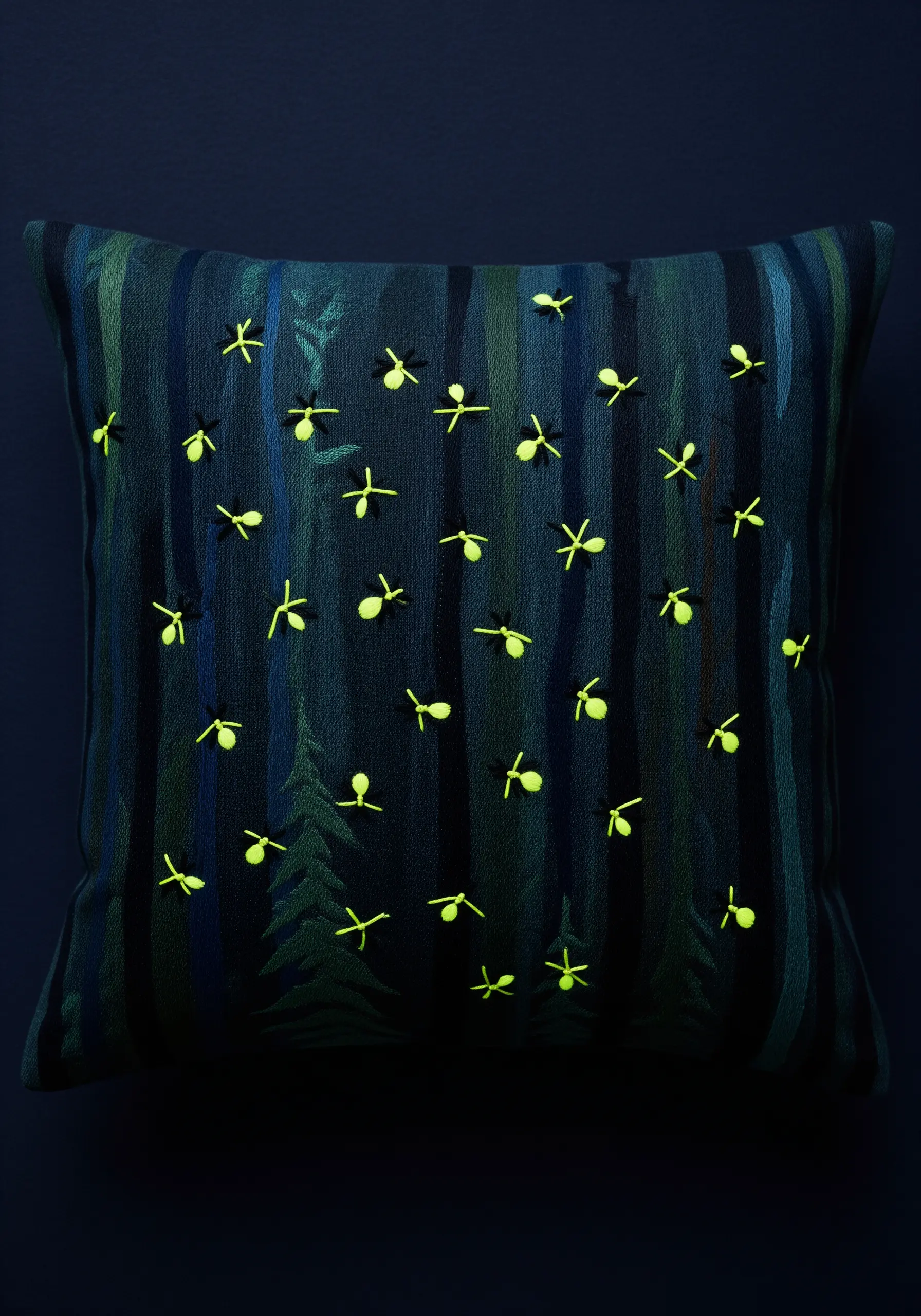 A dark pillow with an embroidered night forest scene dotted with glowing yellow fireflies.