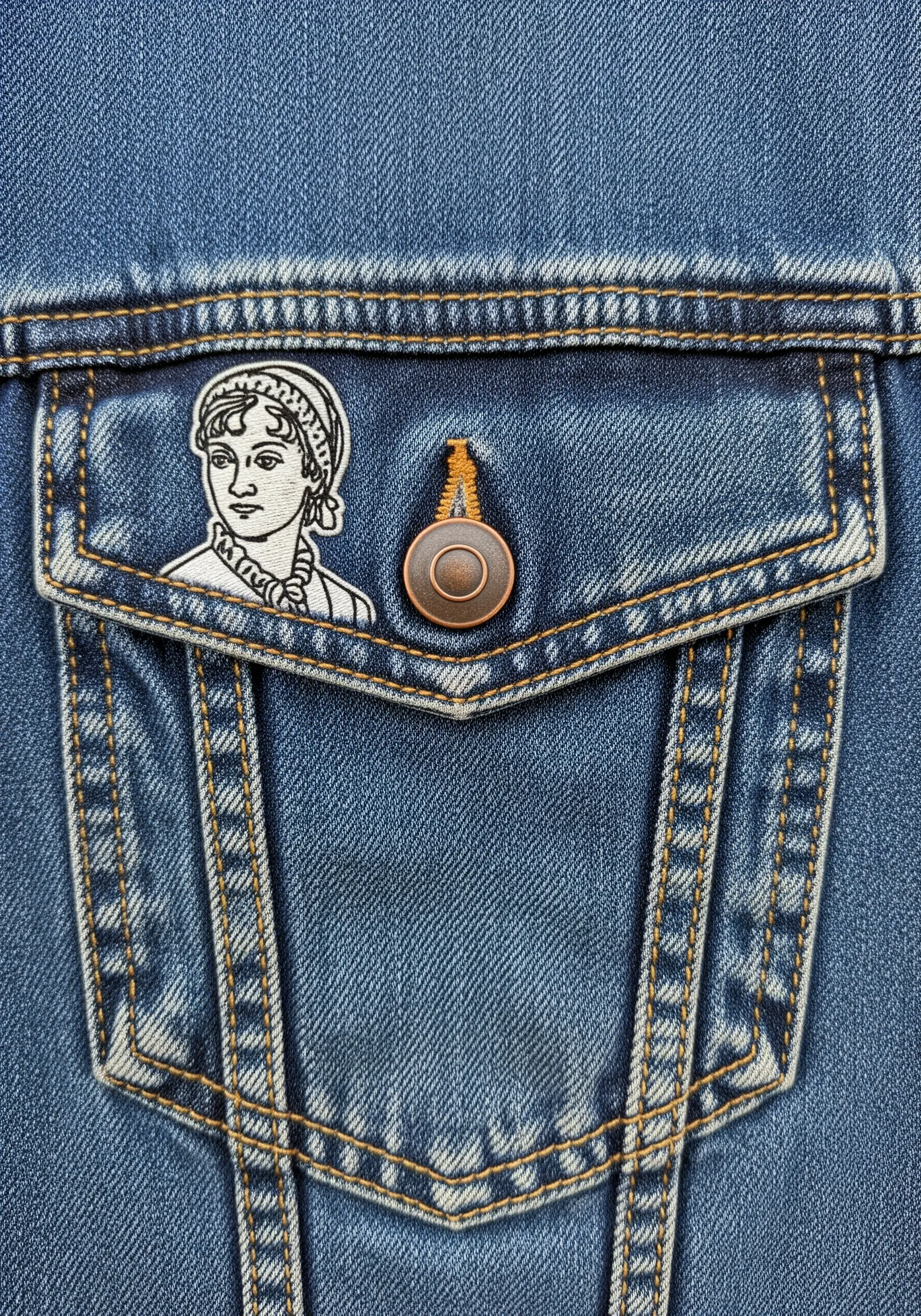 A tiny, detailed line-art portrait patch stitched on the pocket flap of a denim jacket.