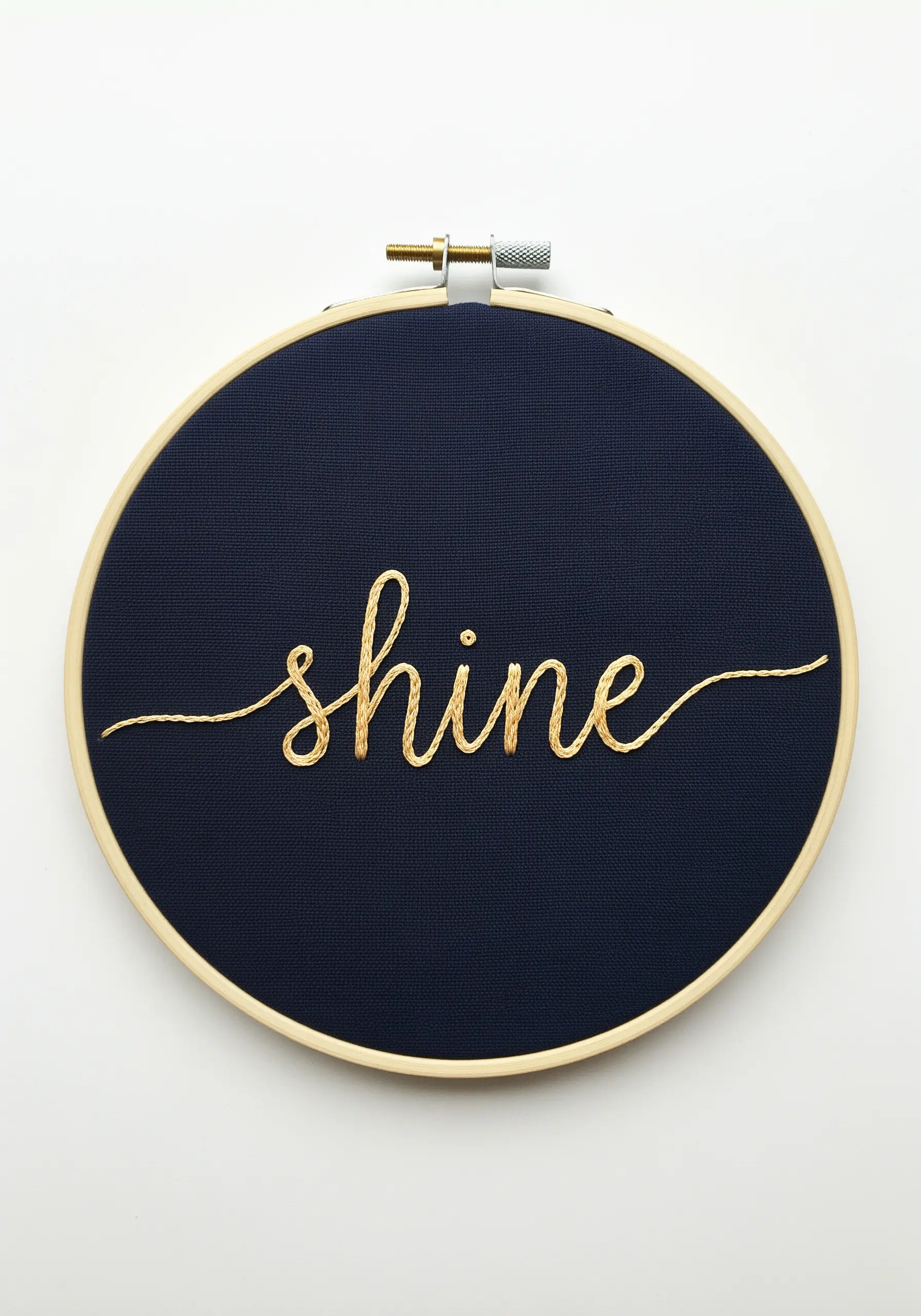 The word 'shine' in flowing gold metallic thread on dark navy fabric.