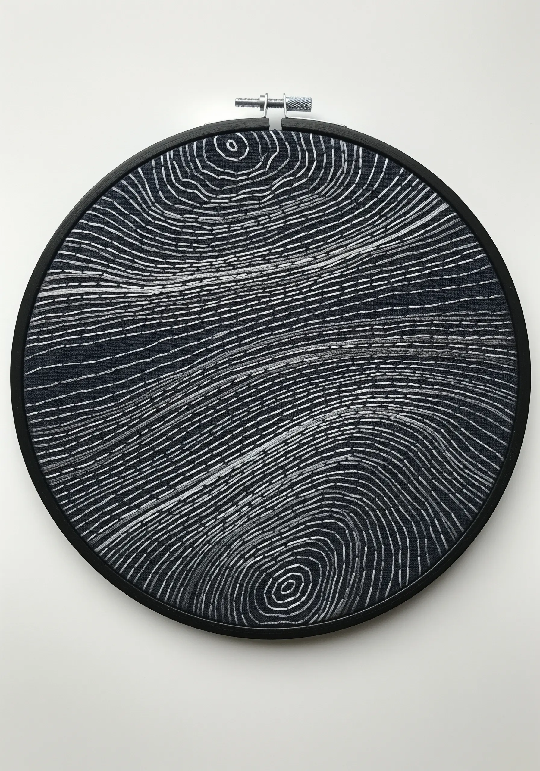 Abstract topographic pattern in white running stitch on black fabric, mimicking wood grain.