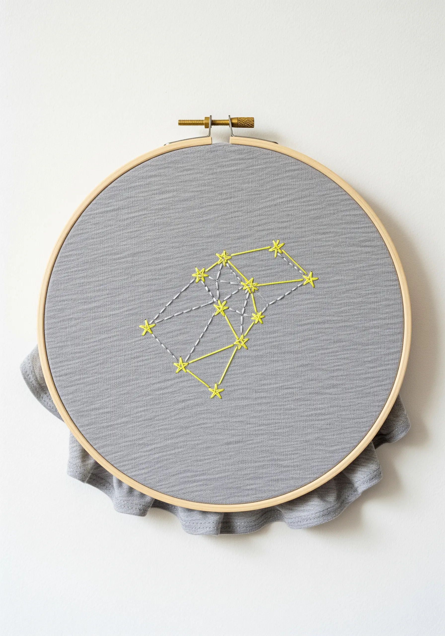 A minimalist constellation stitched in neon yellow thread on gray fabric in an embroidery hoop.