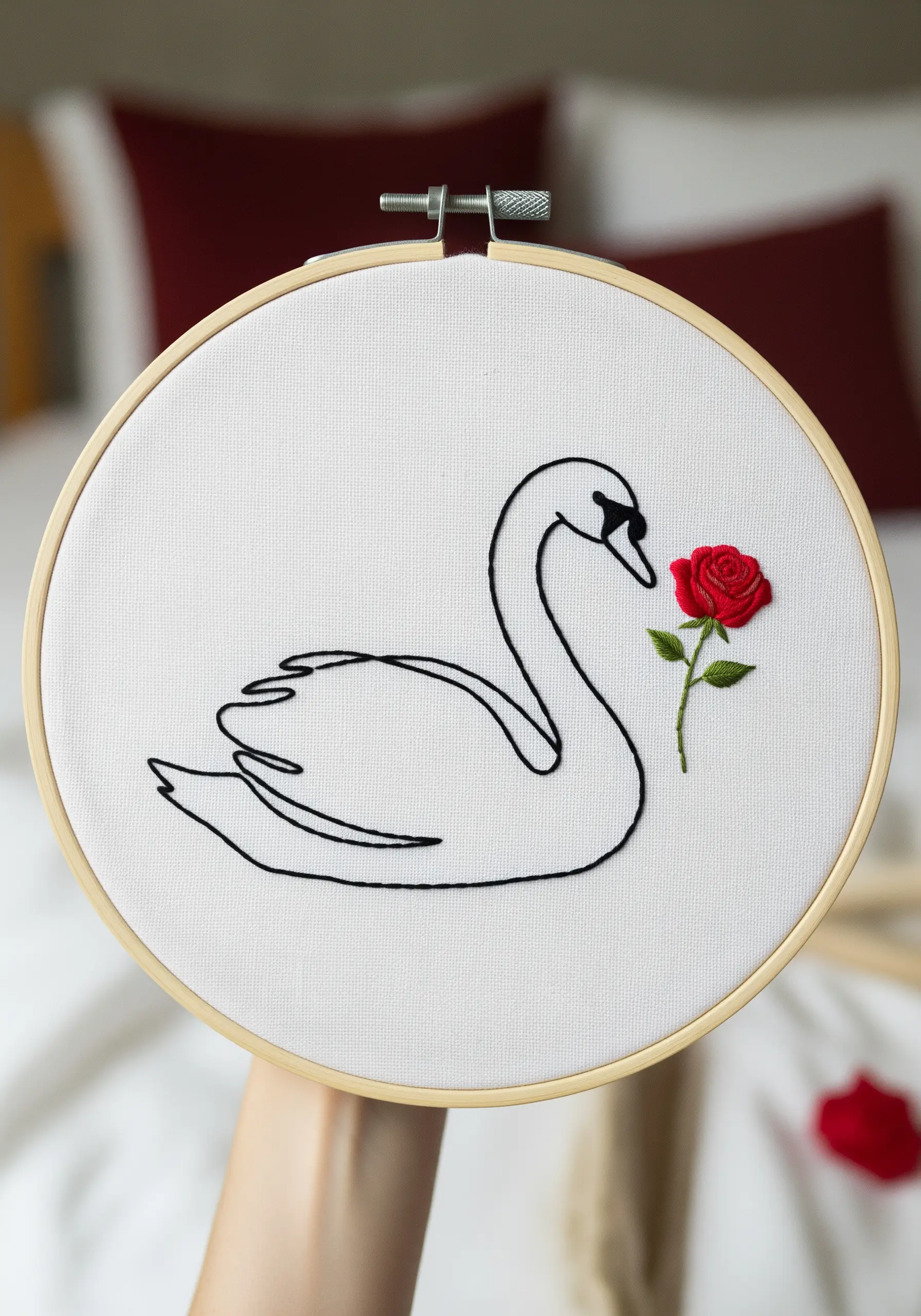 Minimalist line-art embroidery of a swan with a single, dimensional red woven wheel rose.
