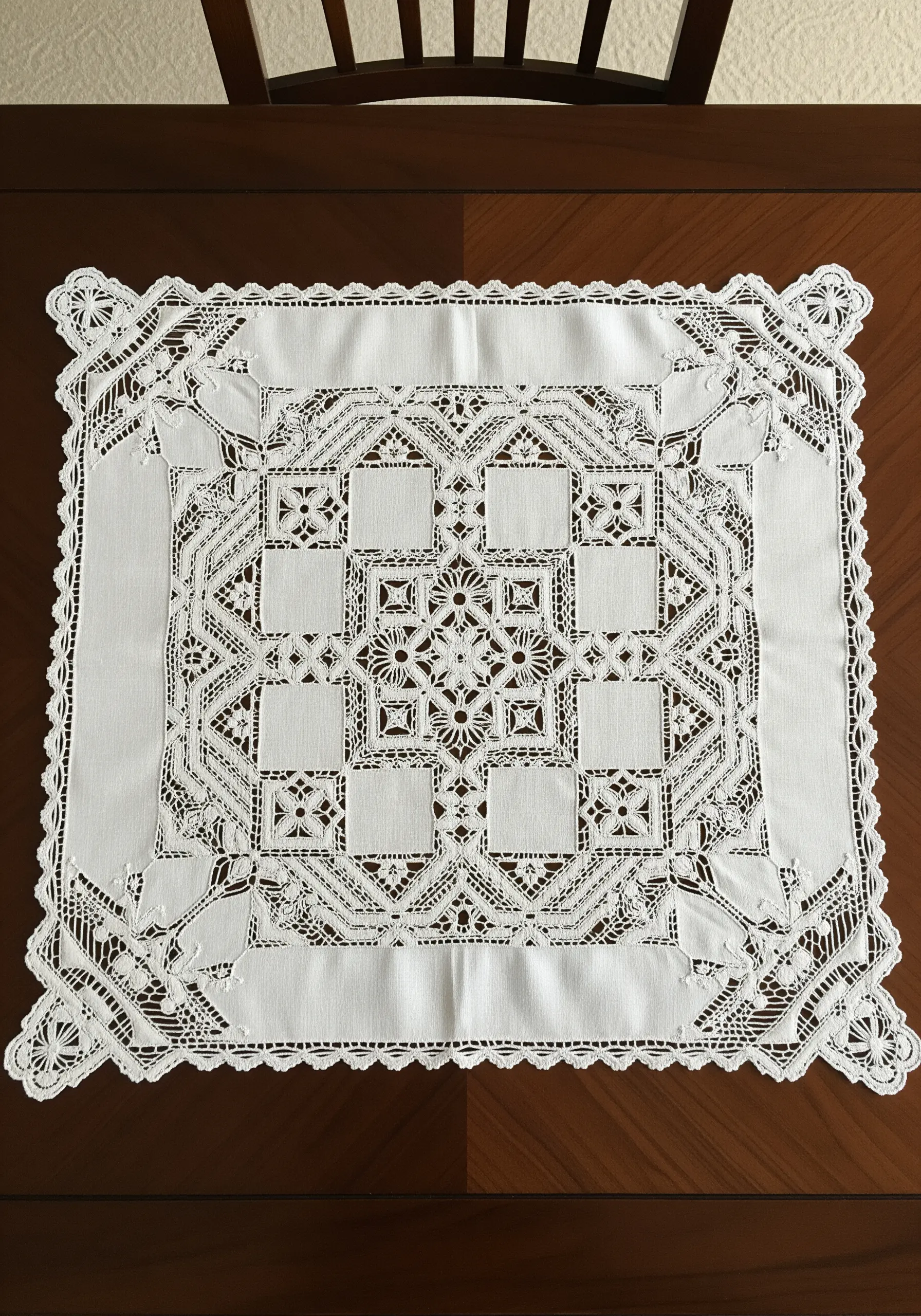 An intricate white-on-white cutwork lace tablecloth with geometric patterns.