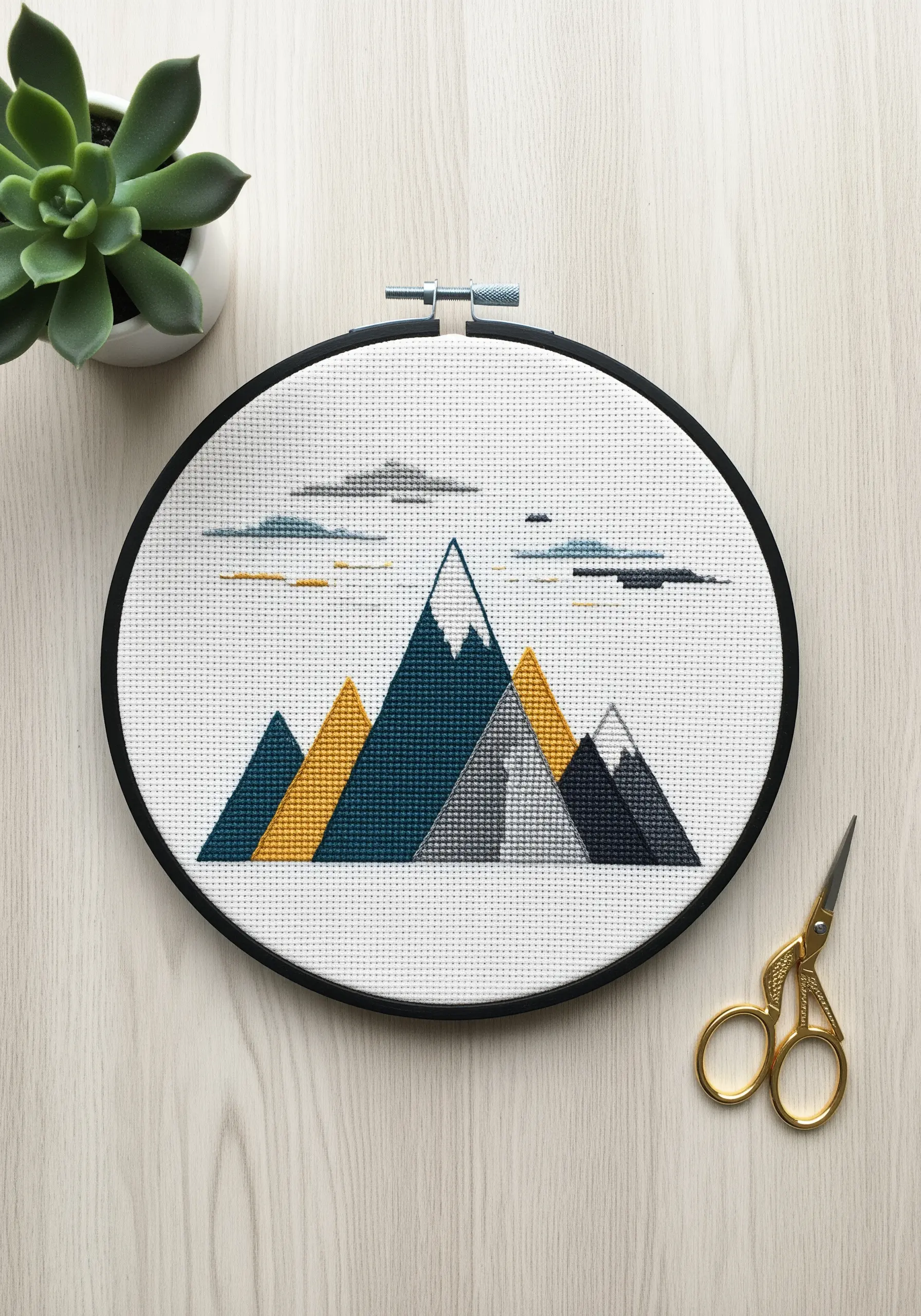 Modern cross-stitch of geometric mountains in teal, mustard, and gray.