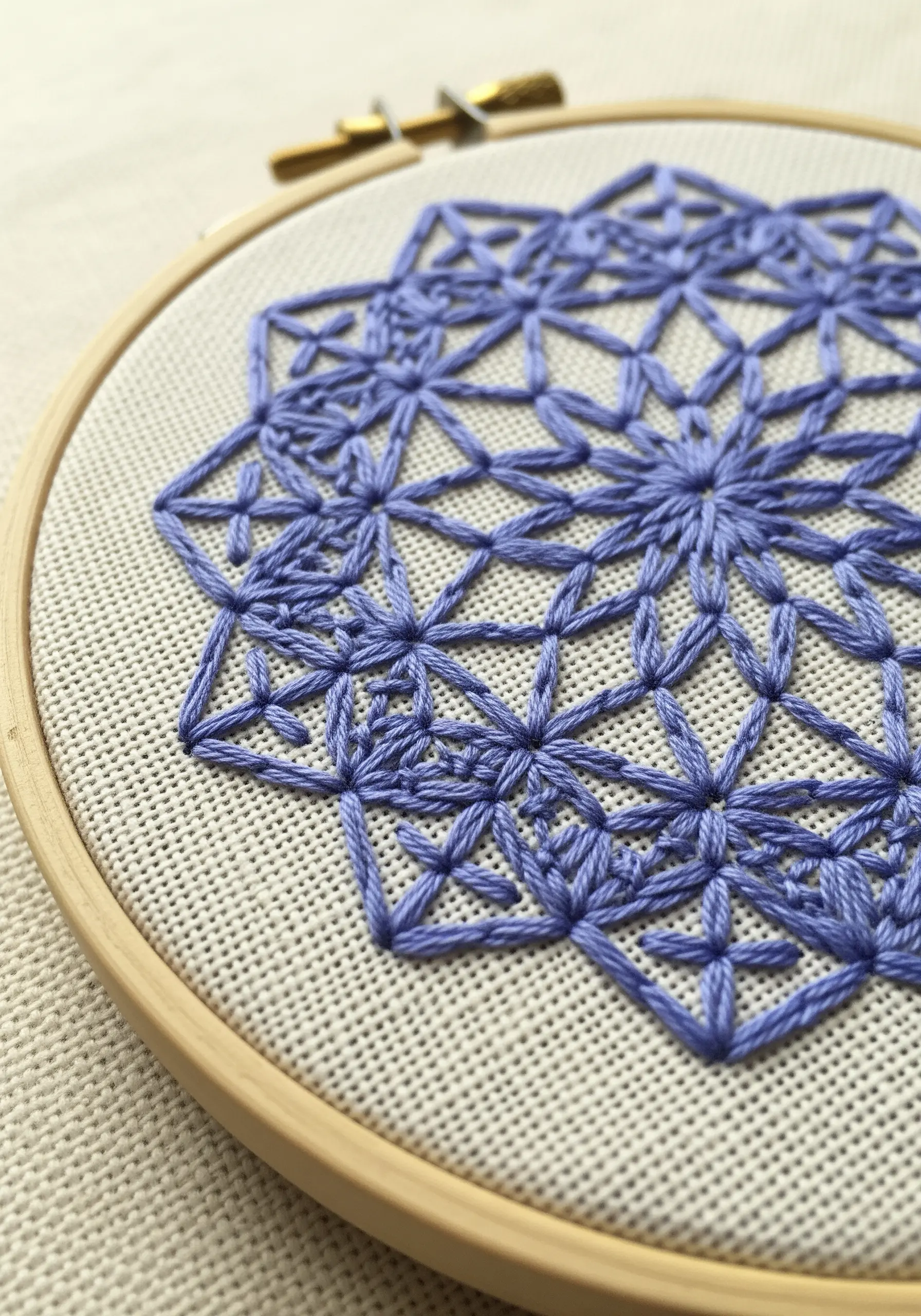 Close-up of a periwinkle geometric lattice stitch mandala in an embroidery hoop.