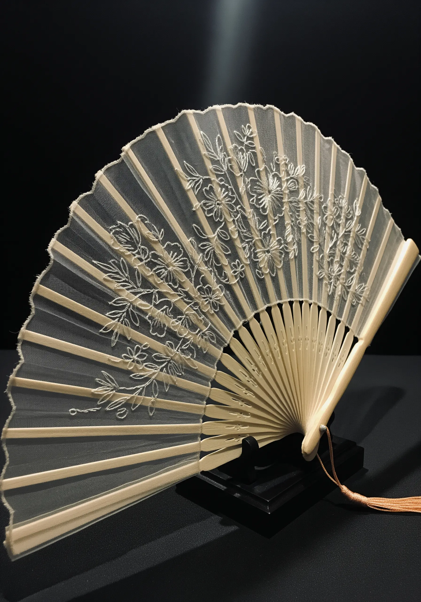 An elegant hand fan made of sheer fabric with delicate white floral embroidery.