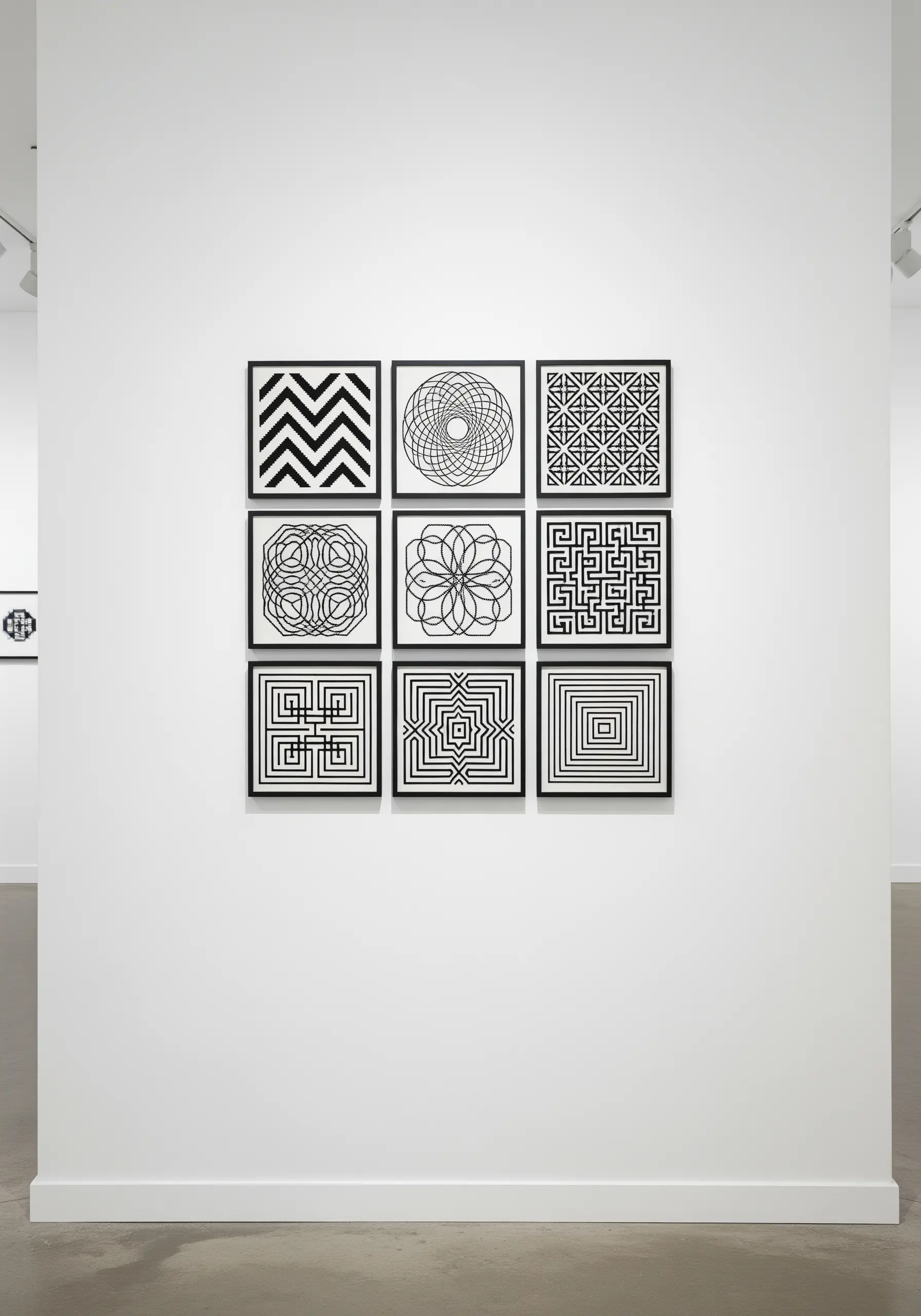 A gallery wall of nine framed black and white geometric embroidery patterns.