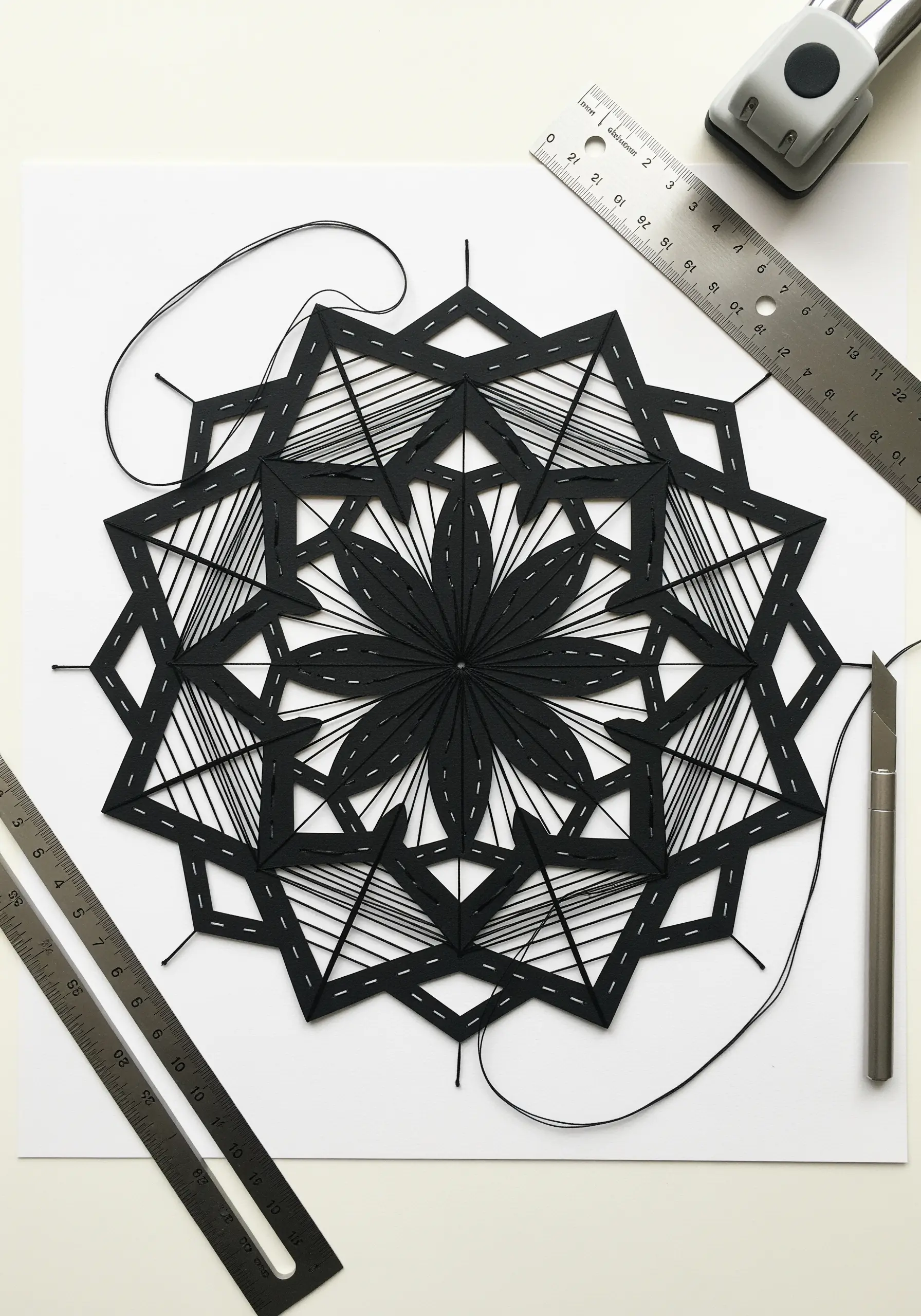 A black geometric mandala created with thread stitched through precisely cut and punched paper.