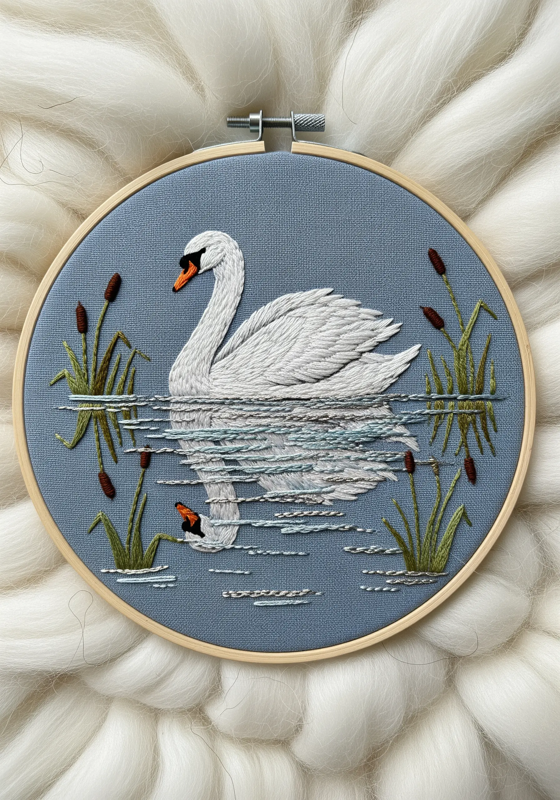 Embroidered swan with its reflection stitched into the water below, surrounded by cattails.