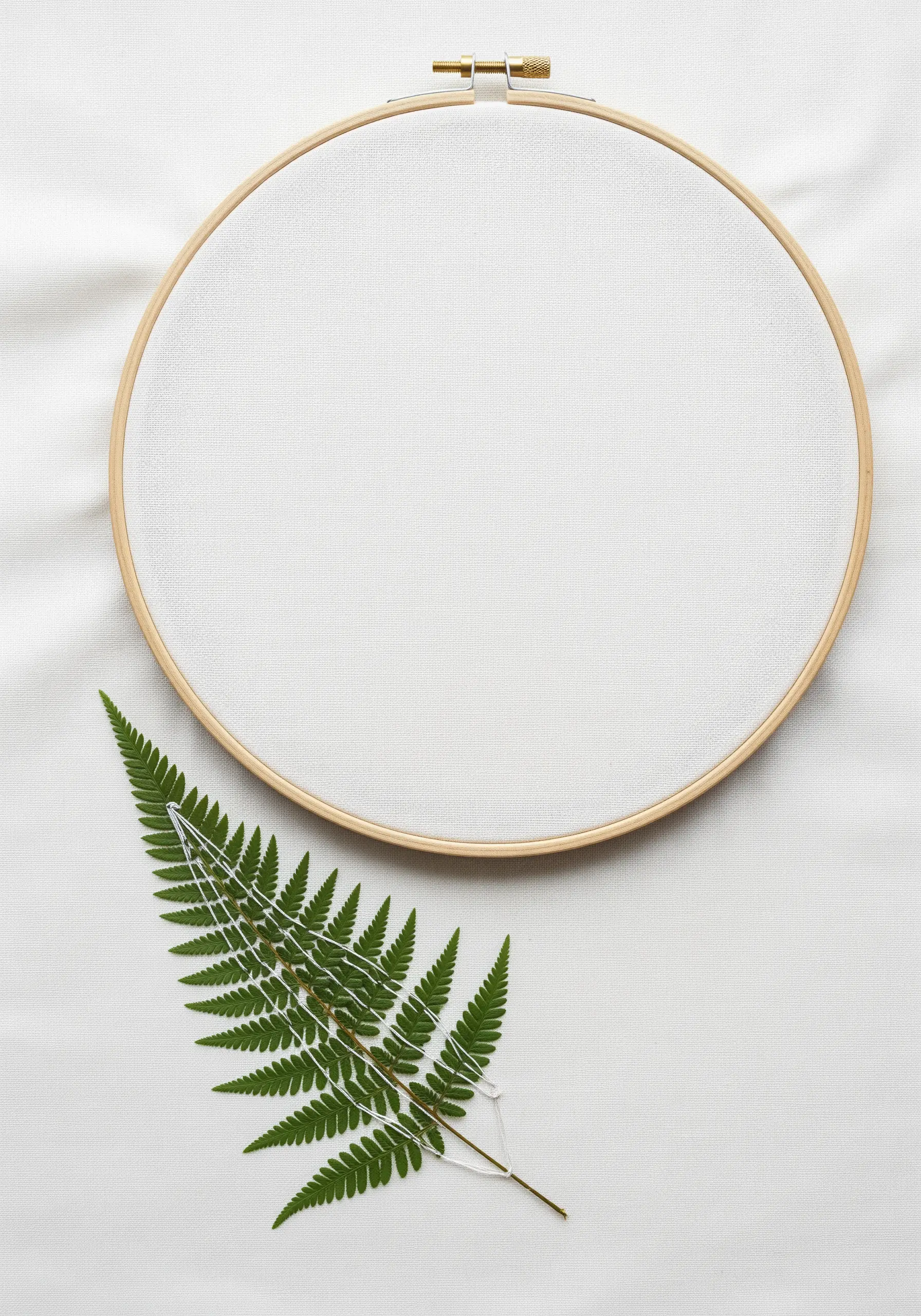 A single pressed fern being carefully stitched onto white fabric in an embroidery hoop.