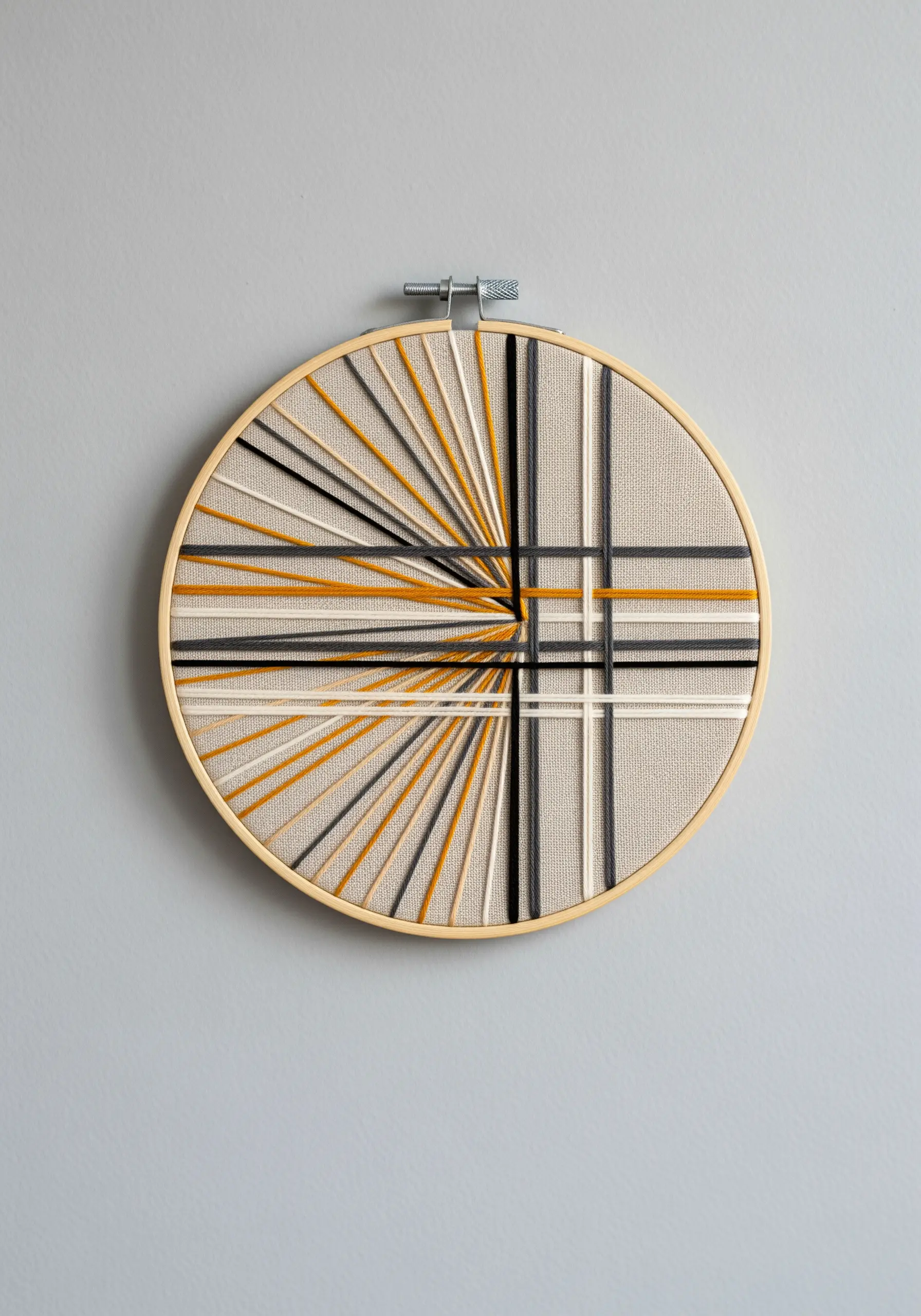Abstract geometric embroidery with wrapped threads in neutral and yellow tones.