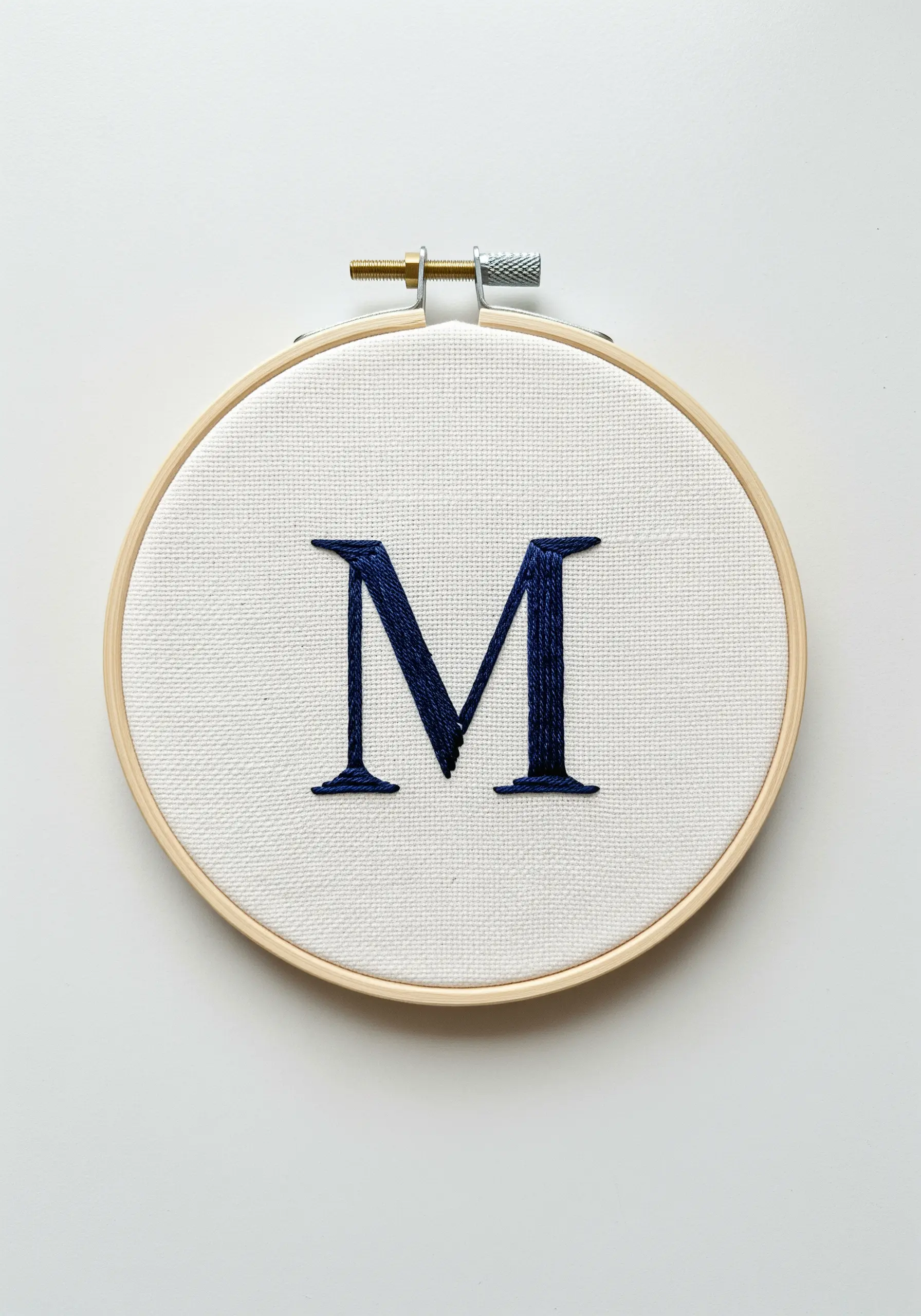 A navy blue serif monogram 'M' in satin stitch on white fabric.
