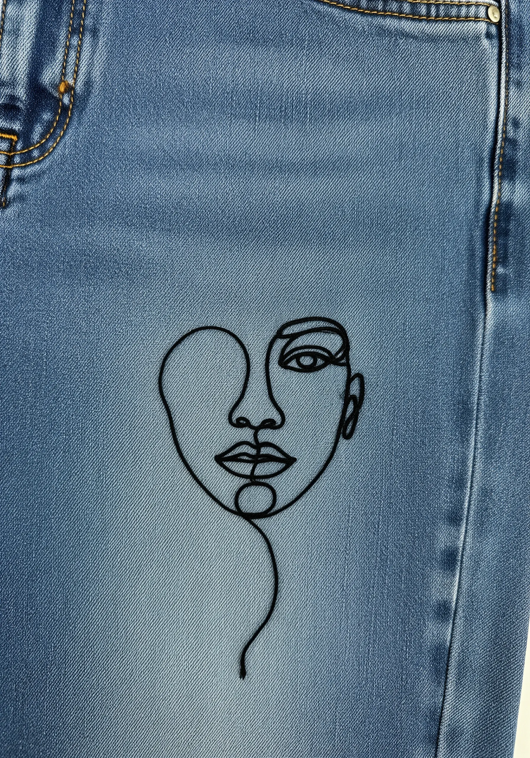 A minimalist single-line art portrait stitched in black thread on medium-wash denim.
