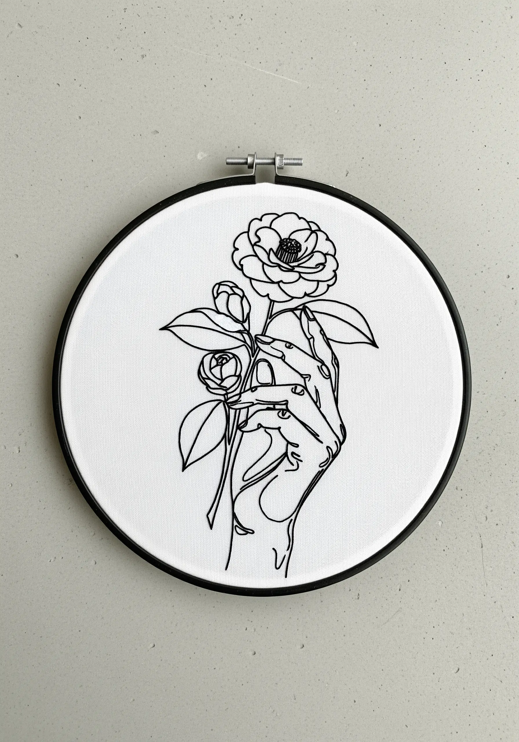 Continuous single line art embroidery of a hand holding a camellia flower.