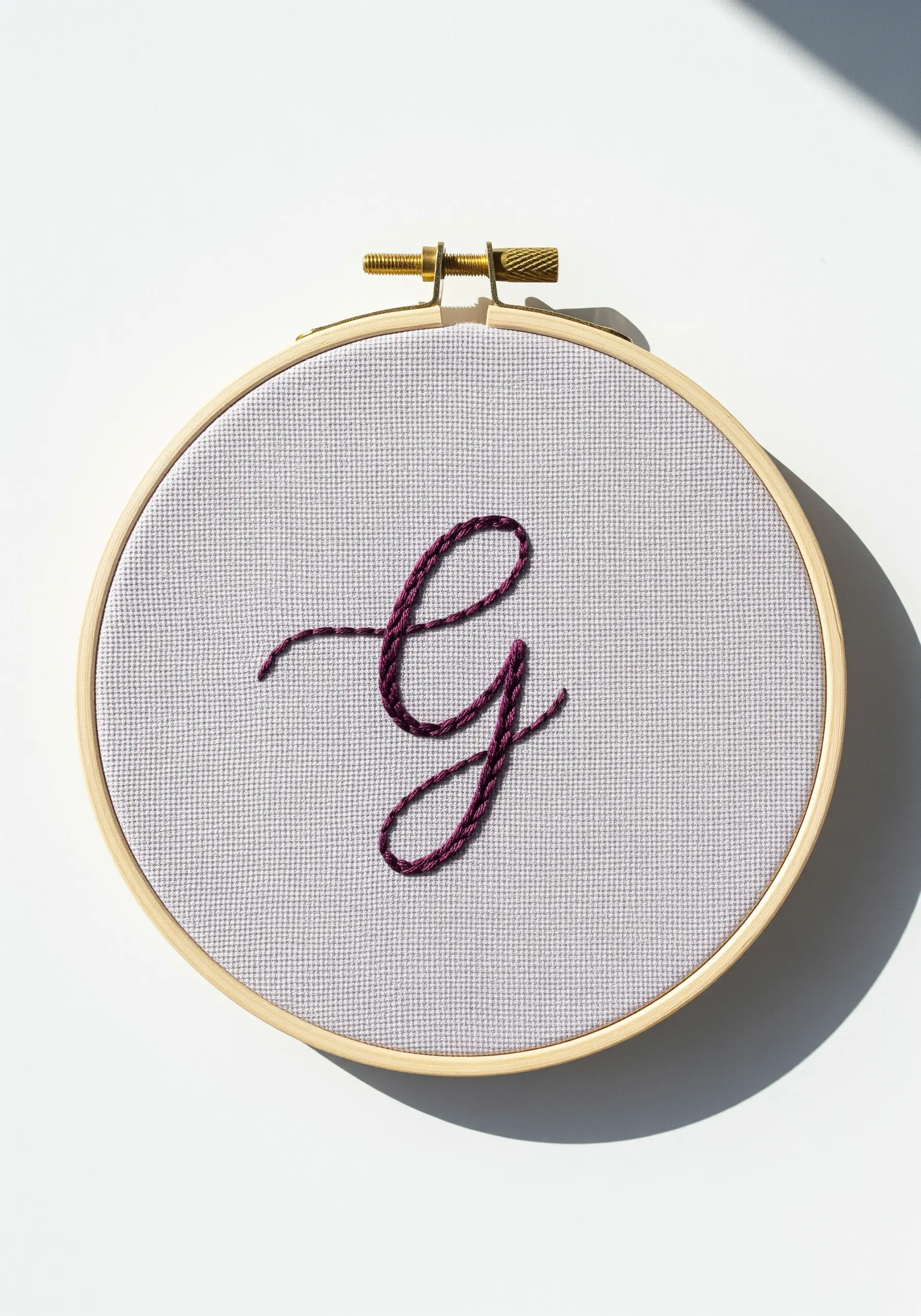 A single, delicate cursive 'g' stitched in dark purple thread.