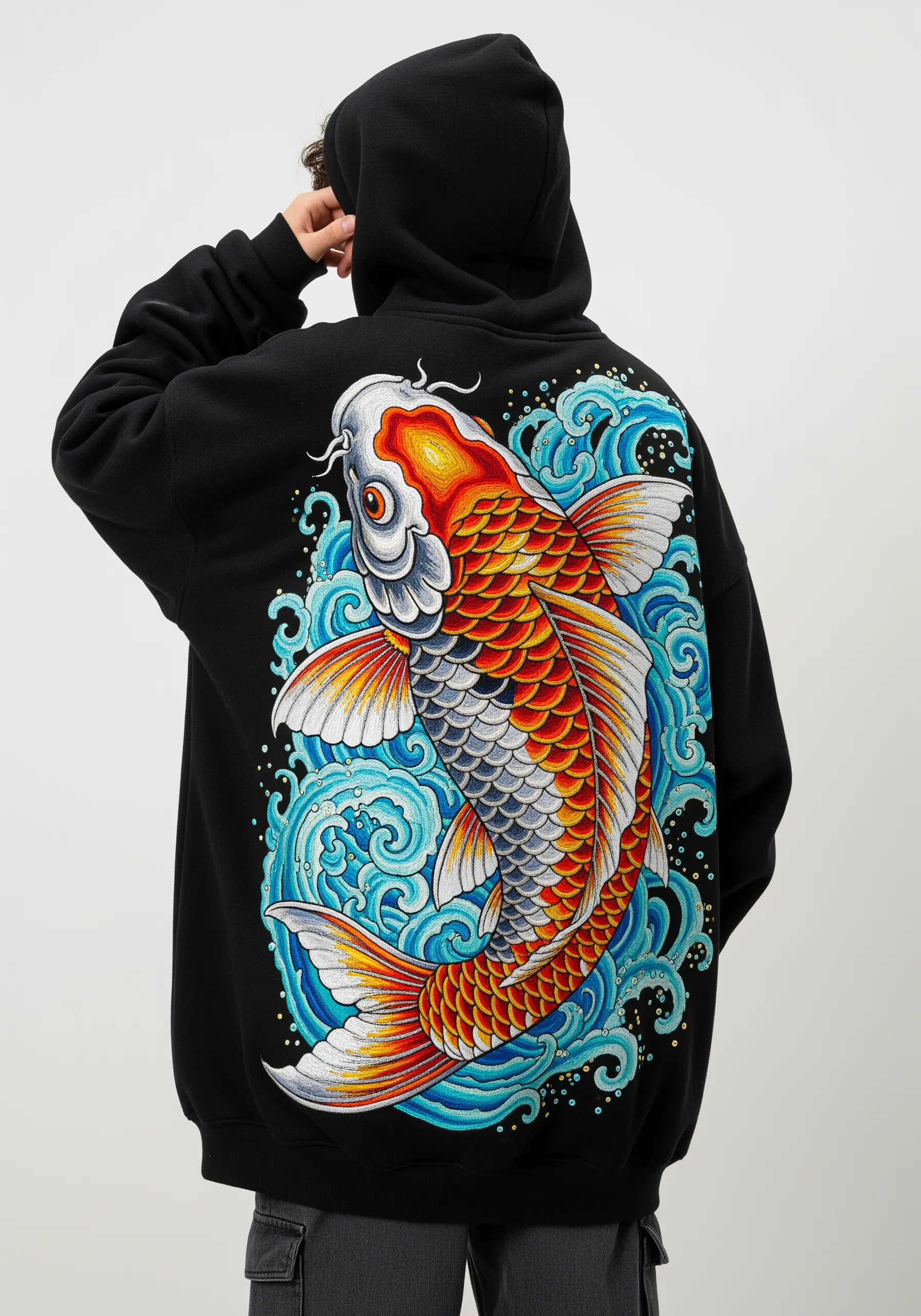 Detailed embroidery of a colorful koi fish and blue waves on the back of a black hoodie.