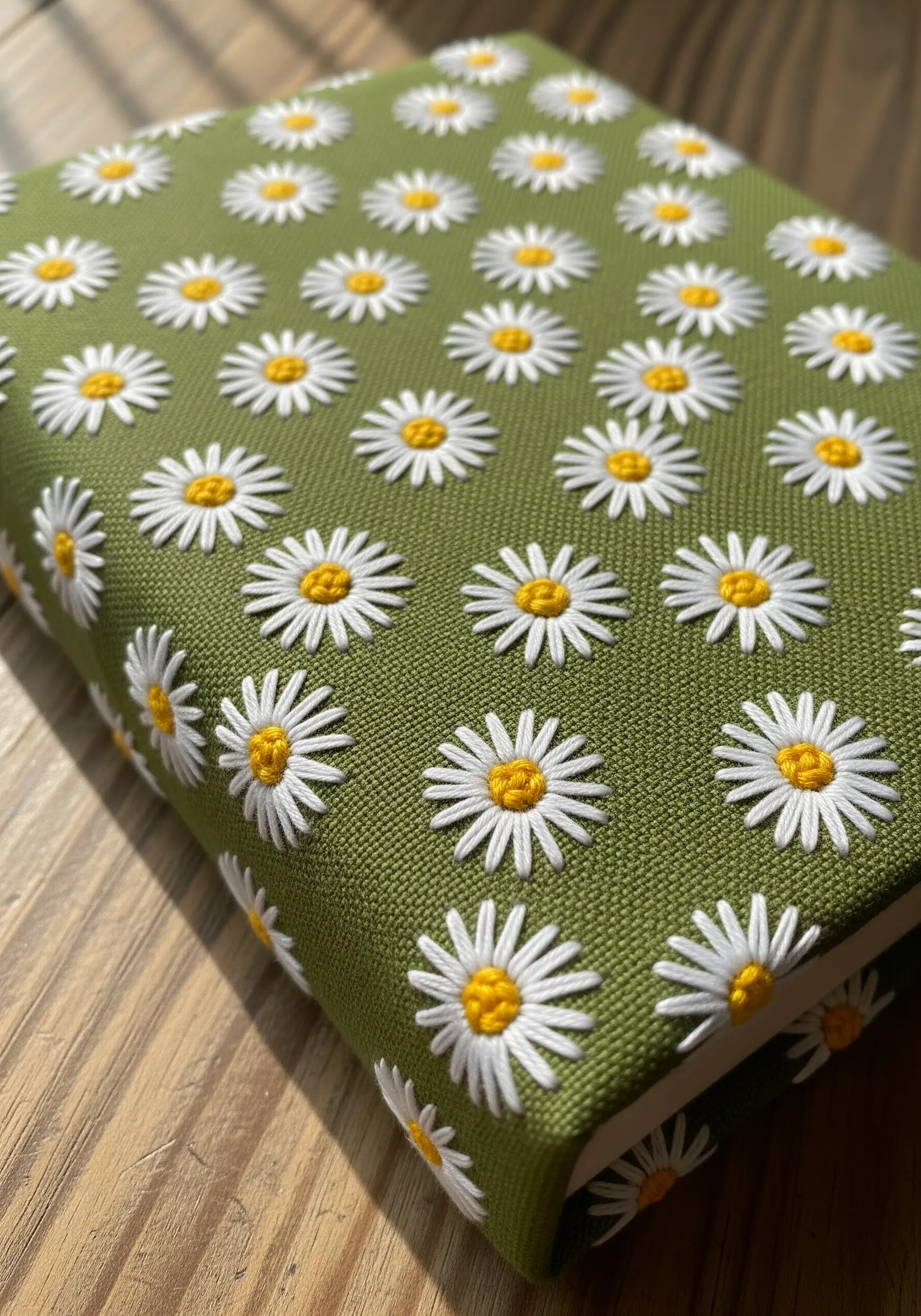A repeating pattern of embroidered daisies on a green fabric book cover.