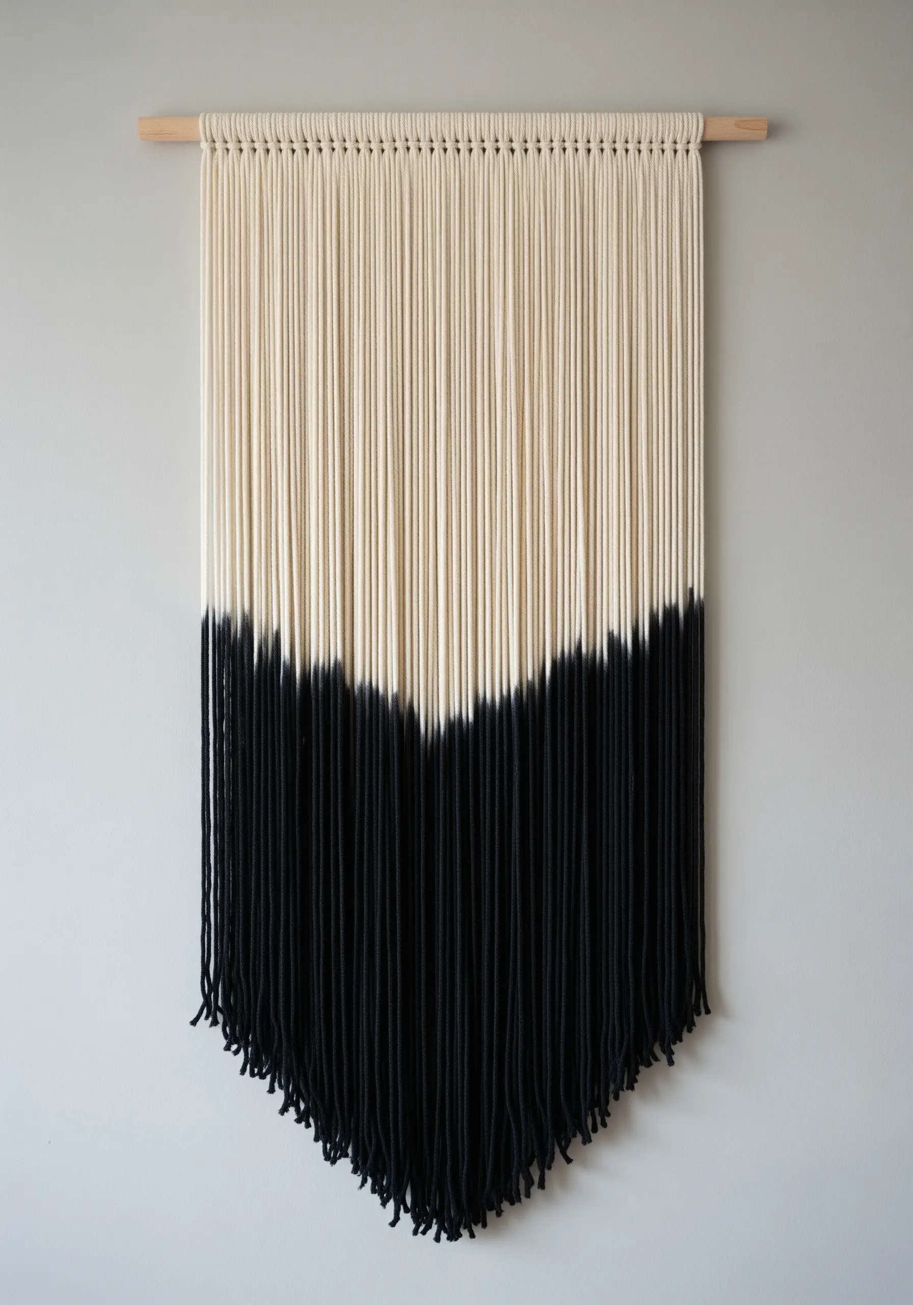 A minimalist wall hanging with cream-colored cords dip-dyed black in a V-shape.