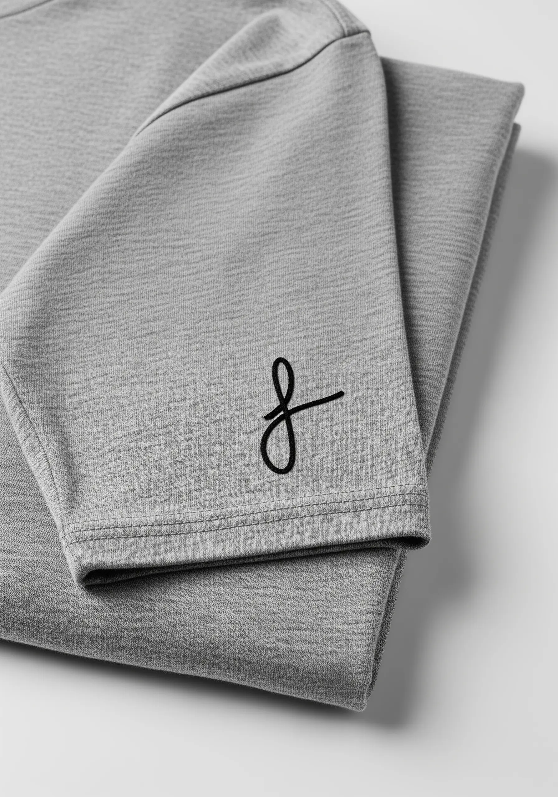 A minimalist, single-line script letter 'f' embroidered in black on a grey t-shirt sleeve.