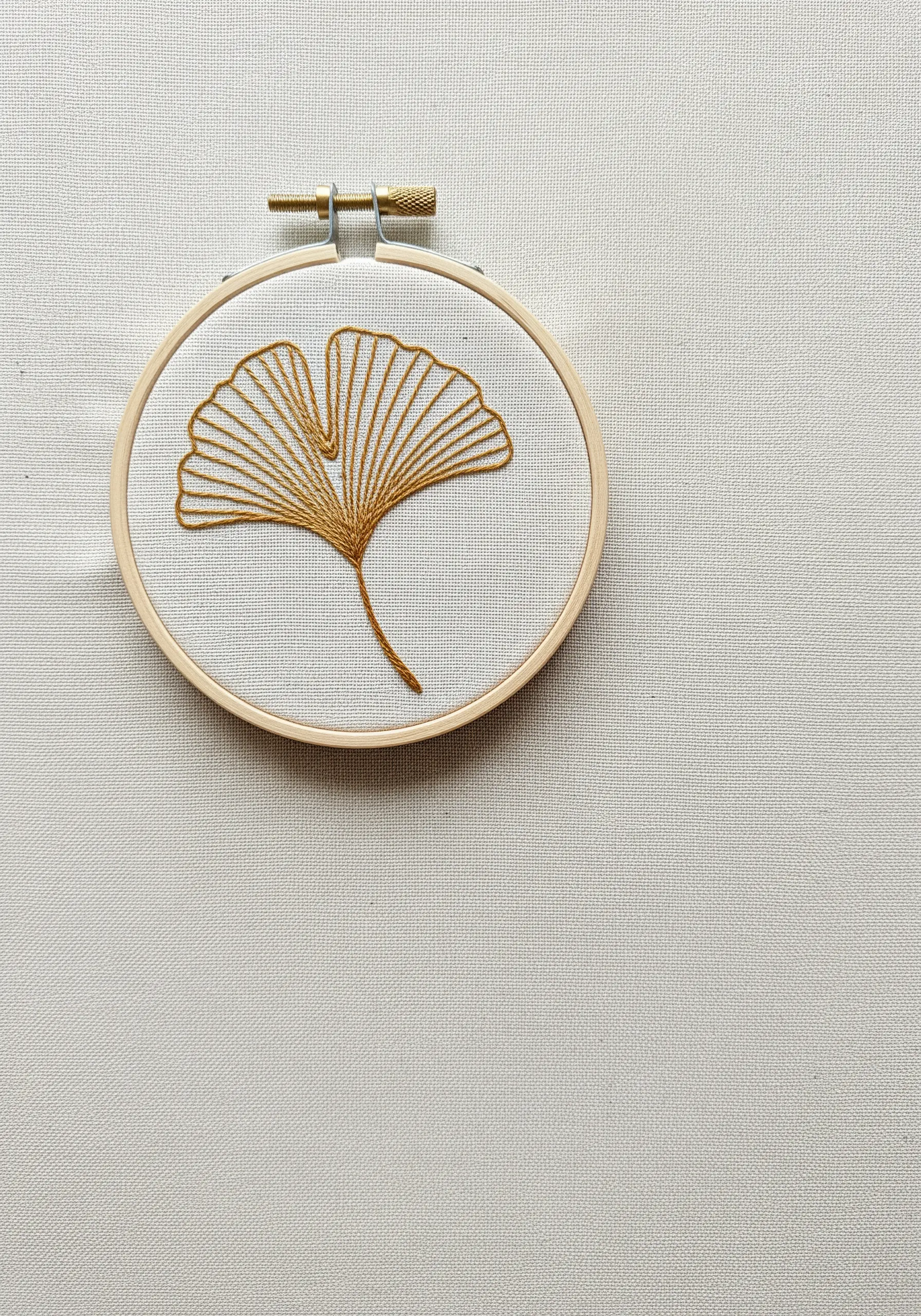Minimalist ginkgo leaf embroidered in golden thread using radiating satin stitch.