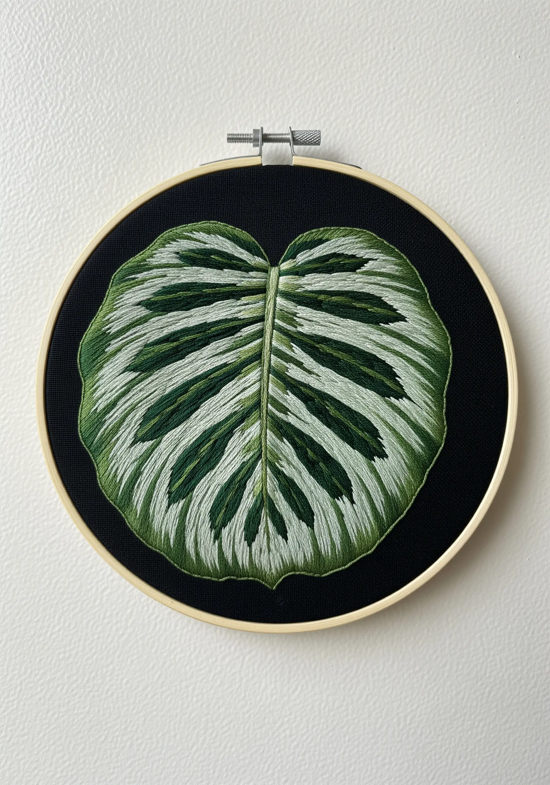 Detailed embroidery of a calathea leaf with white and green stripes on black fabric.
