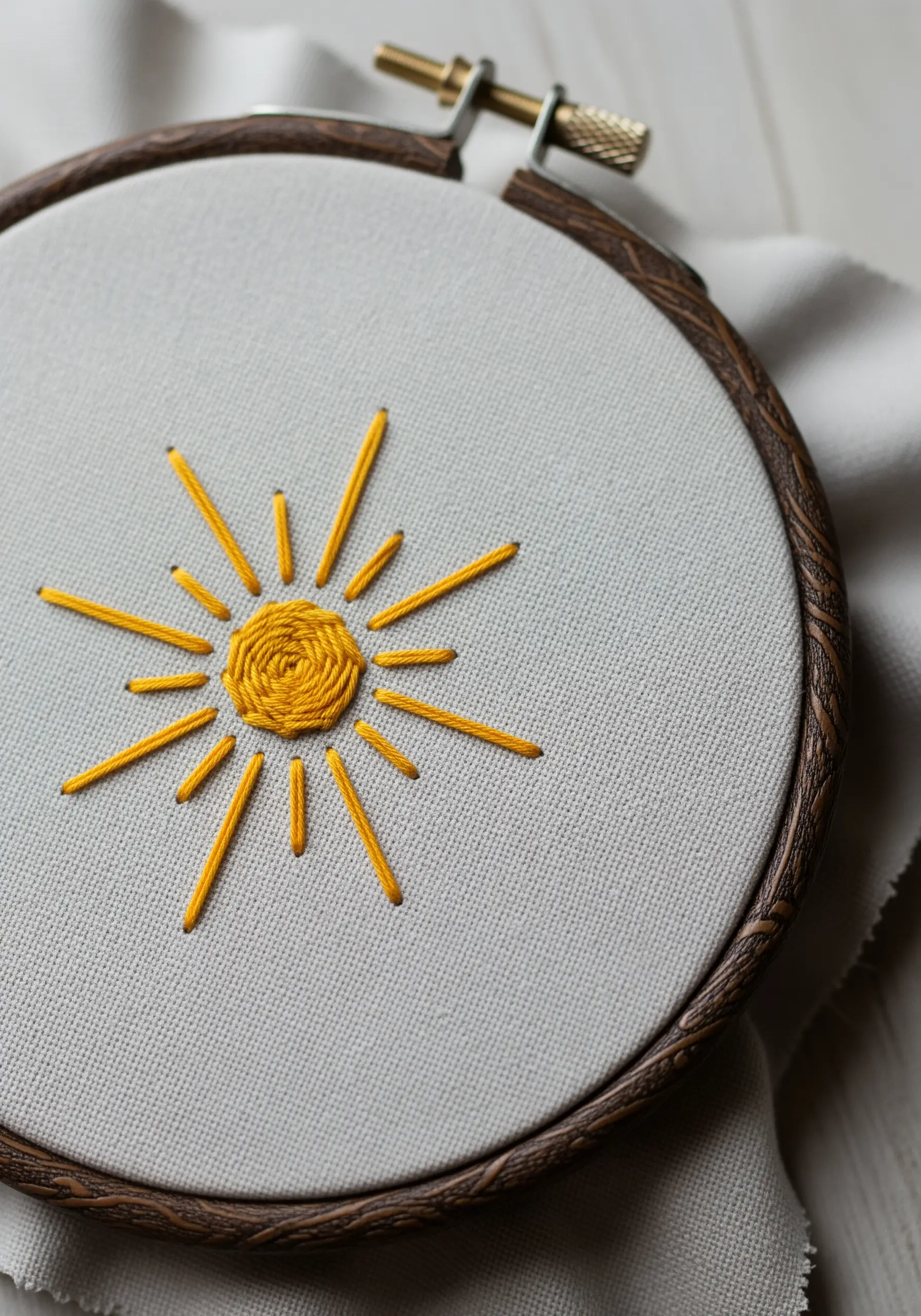 A stylized sun embroidered in yellow thread with a spiral satin stitch center.