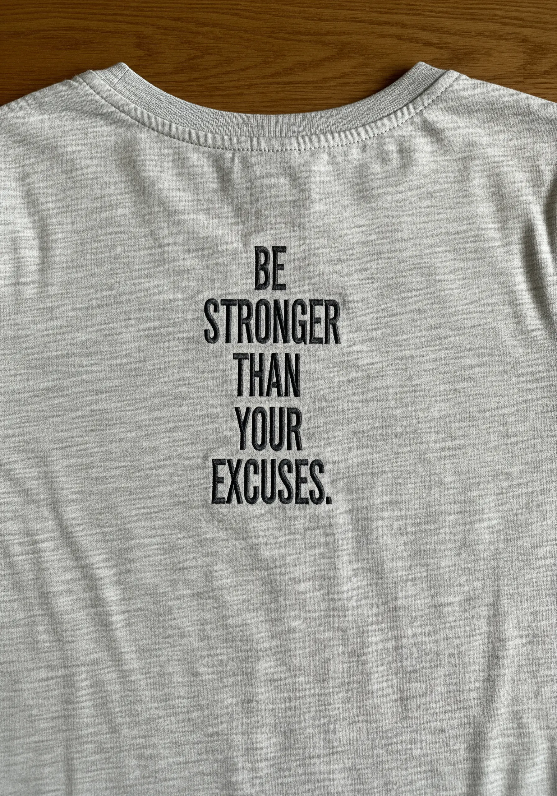 Stacked text “BE STRONGER THAN YOUR EXCUSES” on the back of a grey t-shirt.
