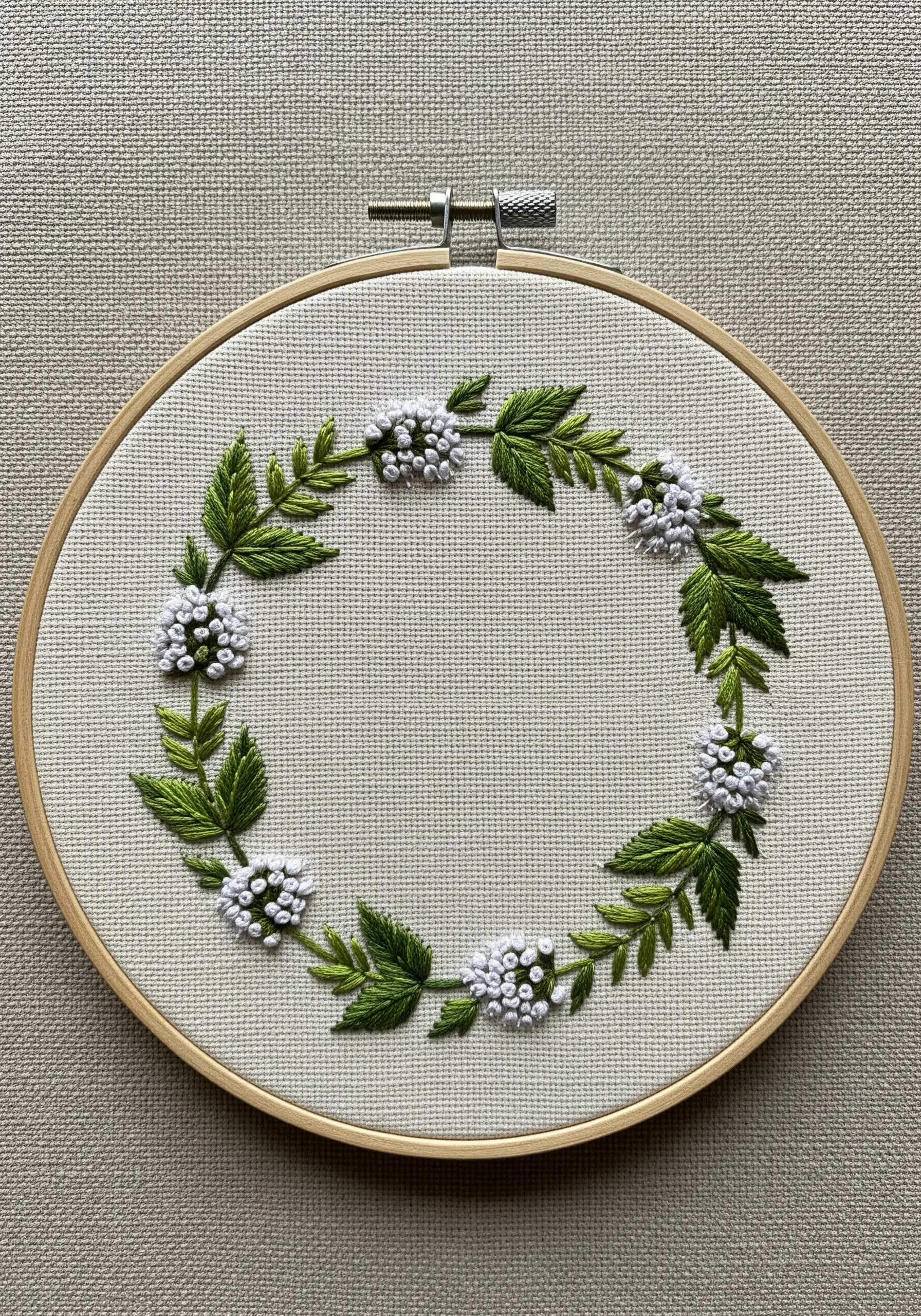 Hand-embroidered wreath of mint leaves and white blossoms in a wooden hoop.
