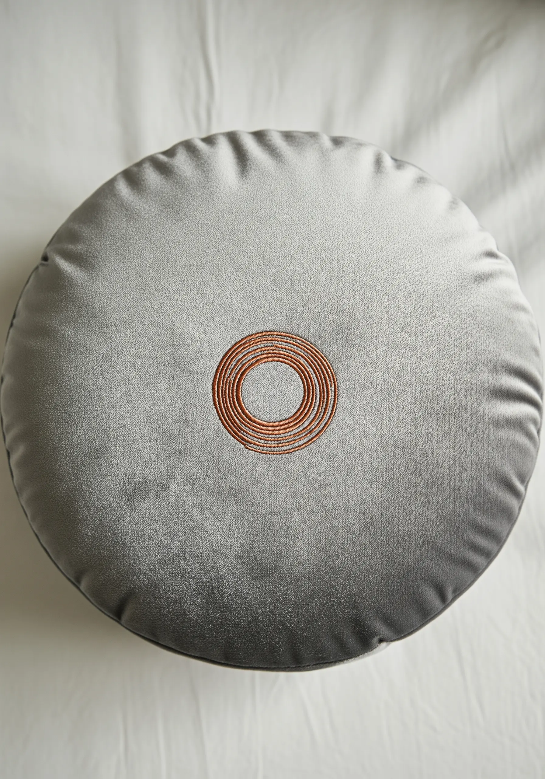 Concentric circles in orange and white satin stitch on a gray velvet cushion.